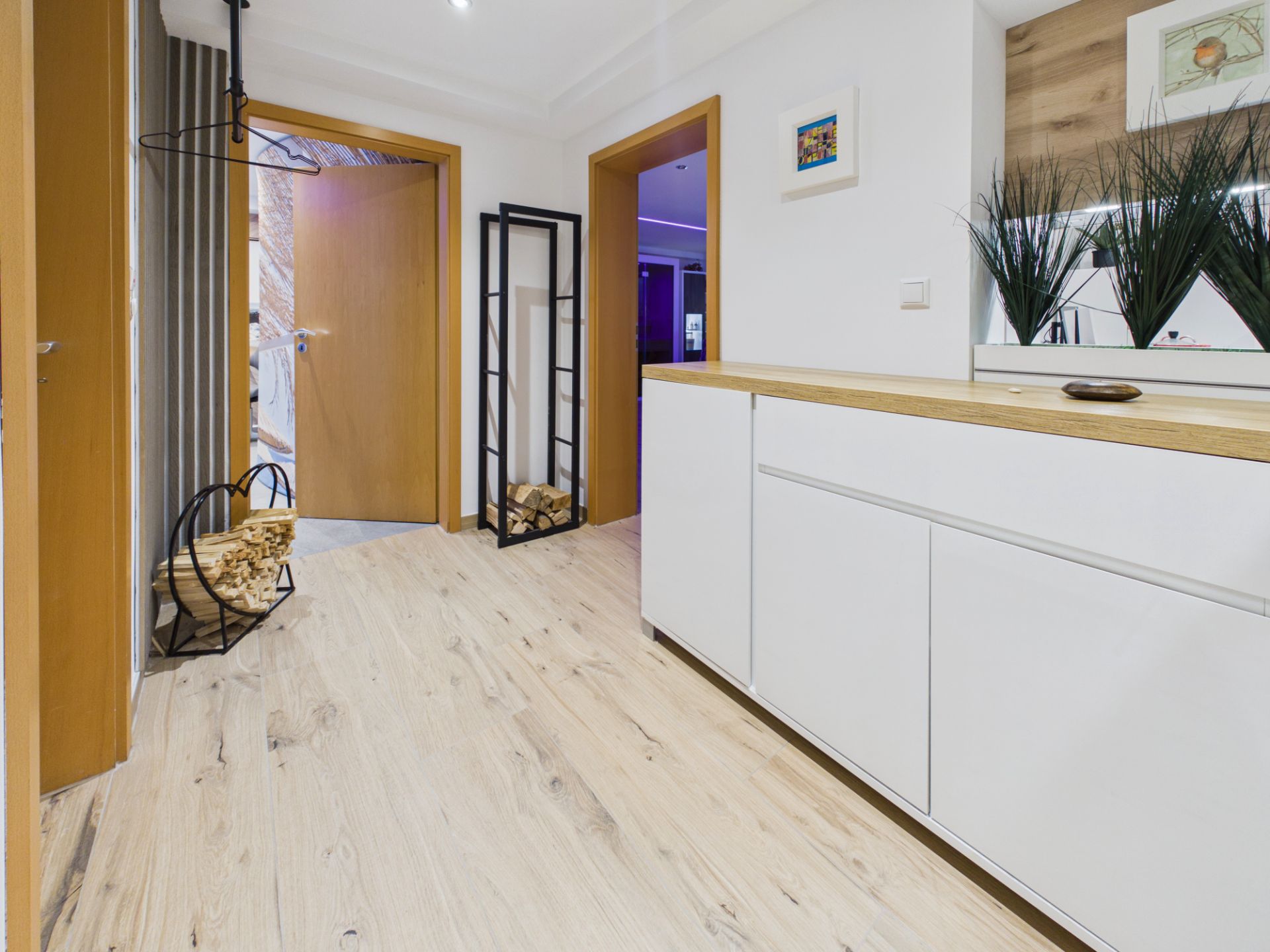 Moderner Flur mit Holzfußboden, weißem Sideboard, Pflanzen und offen stehender Tür.
