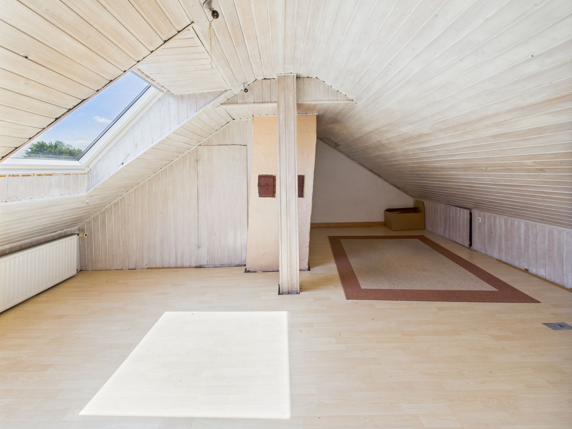 Heller Dachbodenraum mit schrägen Decken, Holzboden und großem Dachfenster.