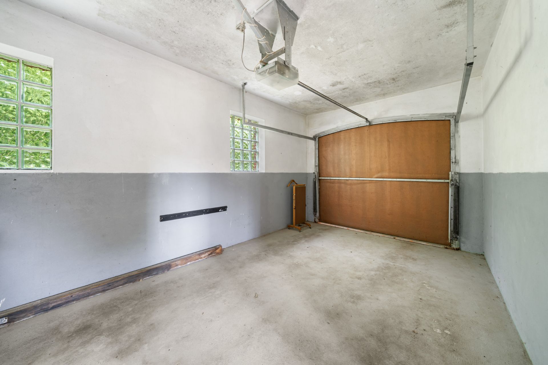 Leere Garage mit braunem Tor und zwei Glasblockfenstern an der linken Wand.