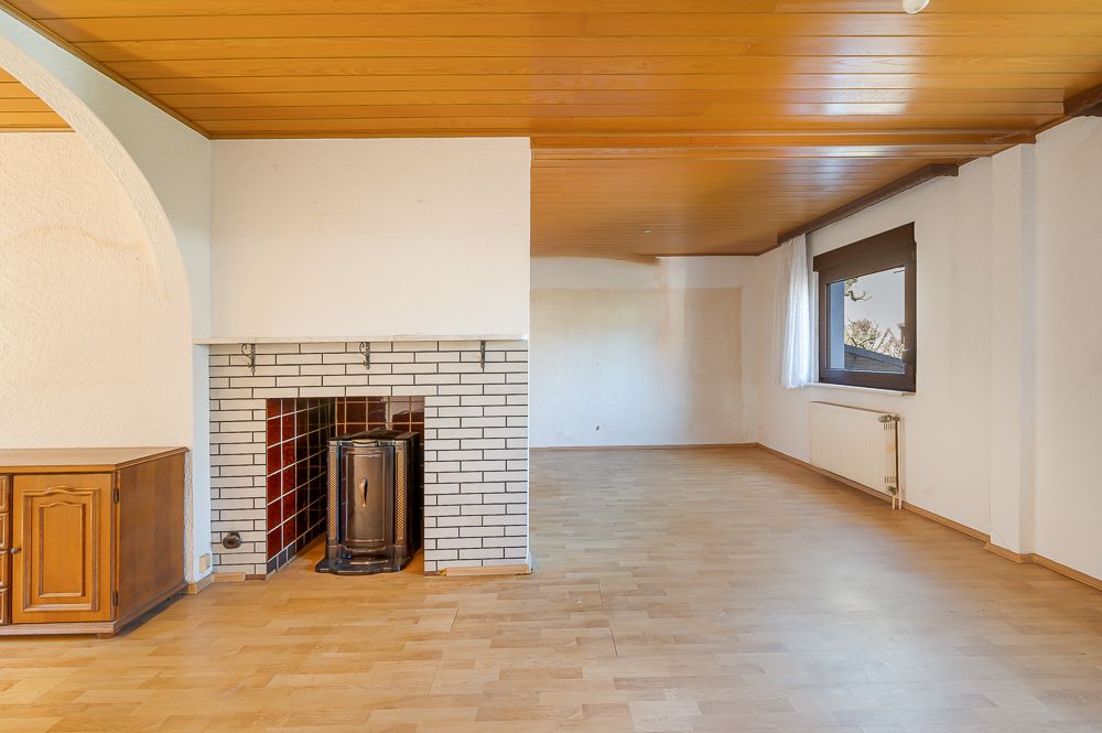 Helles Wohnzimmer mit Holzdecke, Kamin, Parkettboden und großem Fenster.