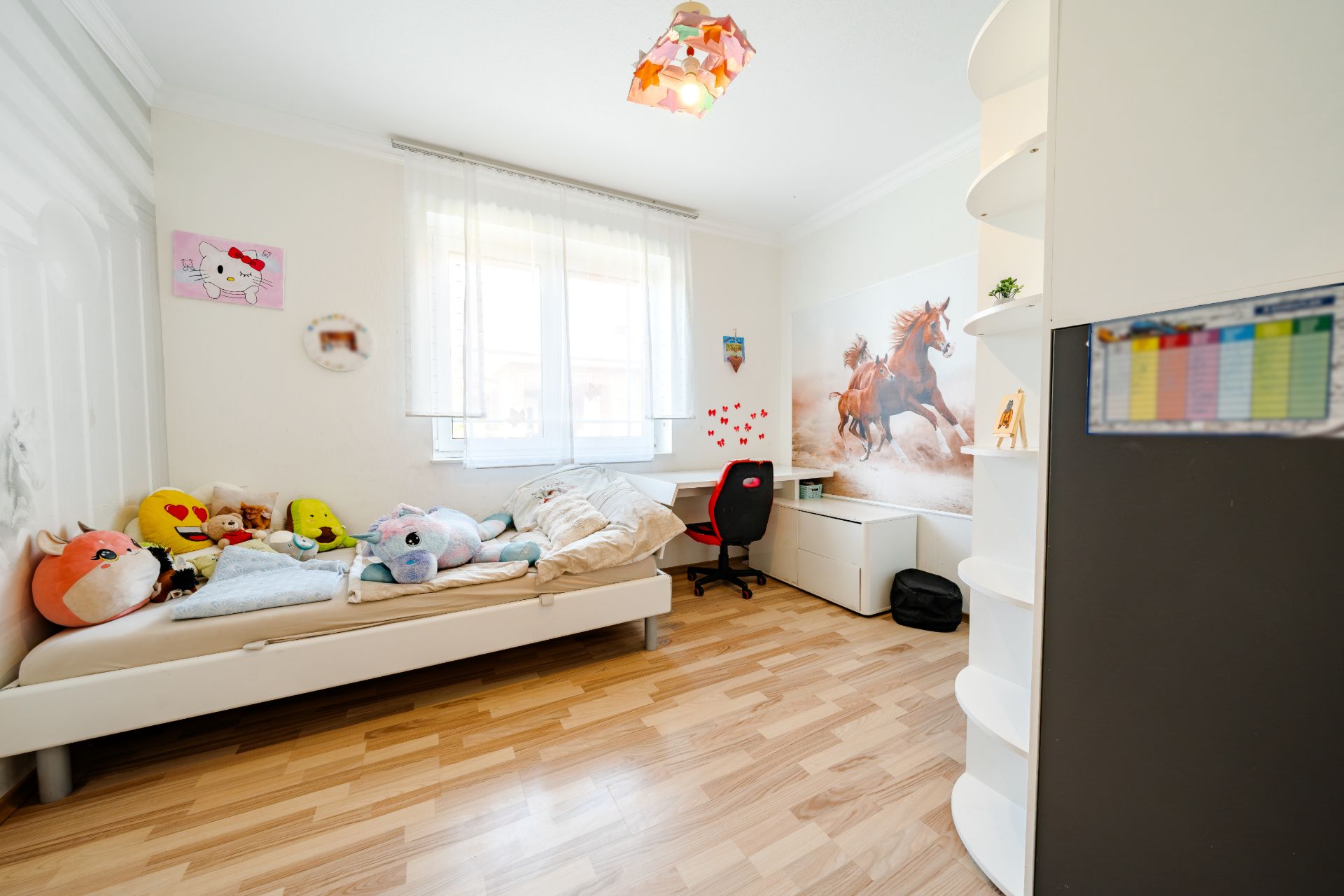 Helles Kinderzimmer mit Einzelbett, Plüschtieren, Schreibtisch und Wandbild von Pferden.