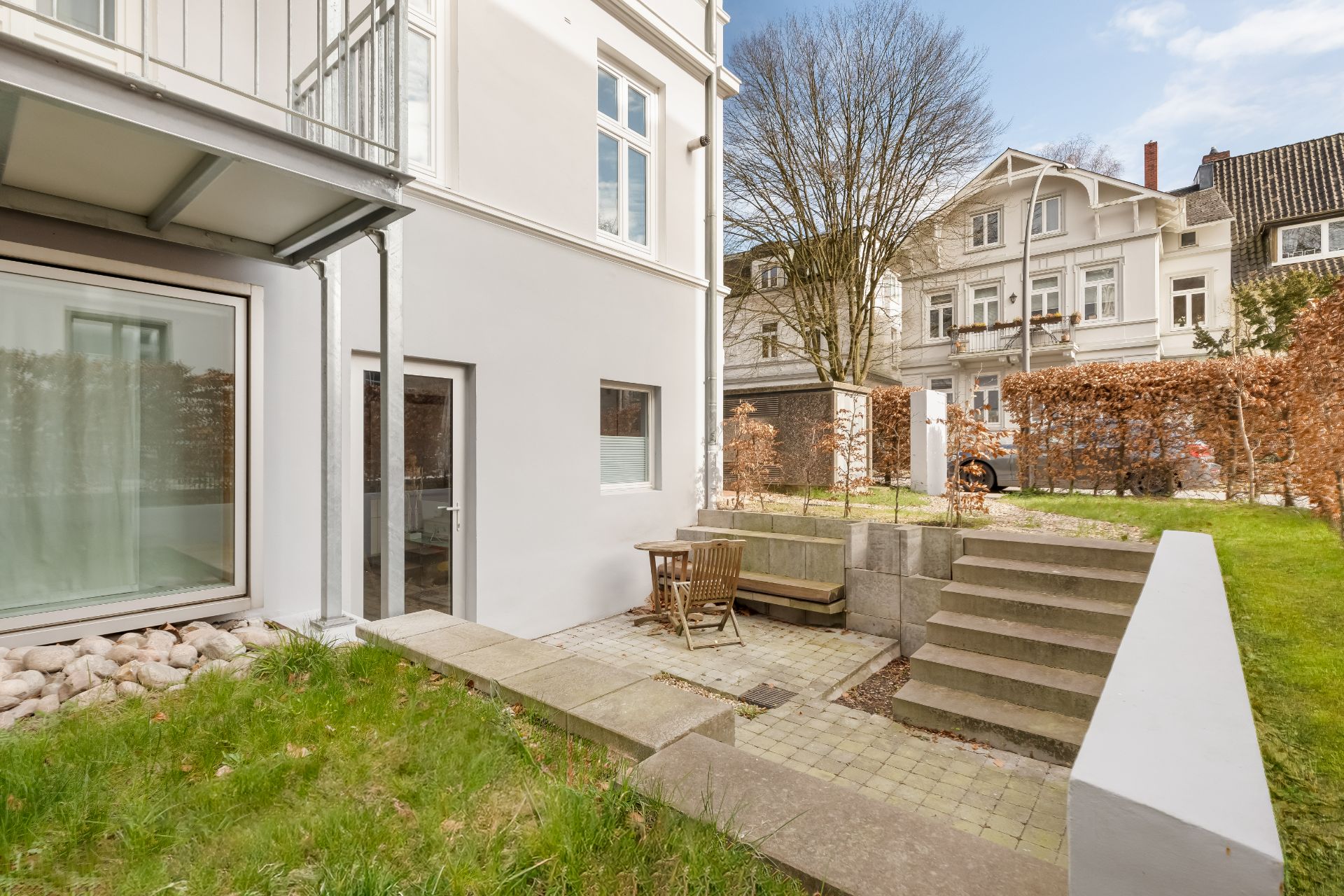 Kleine Terrasse im Garten mit Tisch, Stühlen, Bank und angrenzender Treppe an einem Wohnhaus.