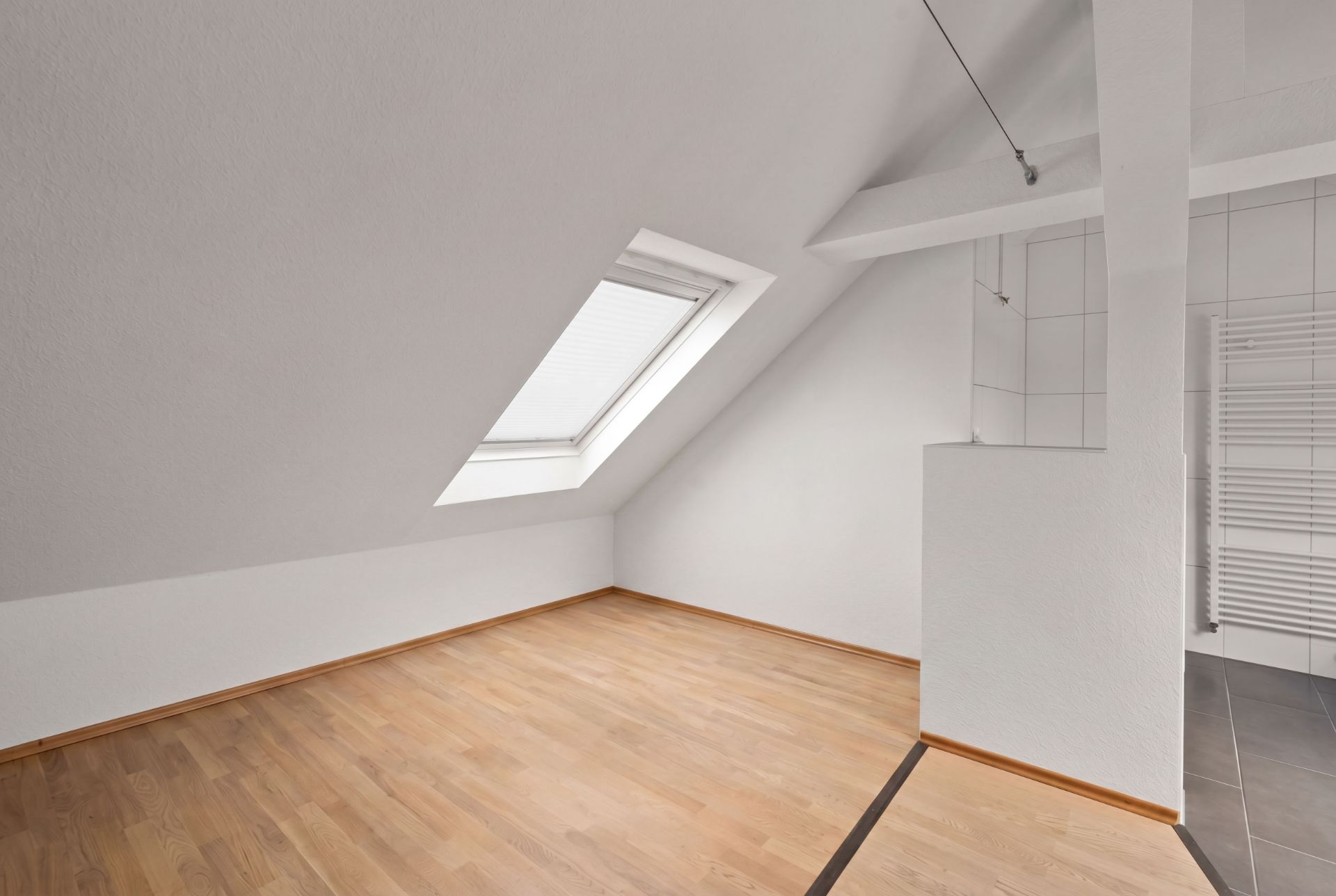 Helles Dachzimmer mit schräger Decke, Dachfenster und Parkettboden.
