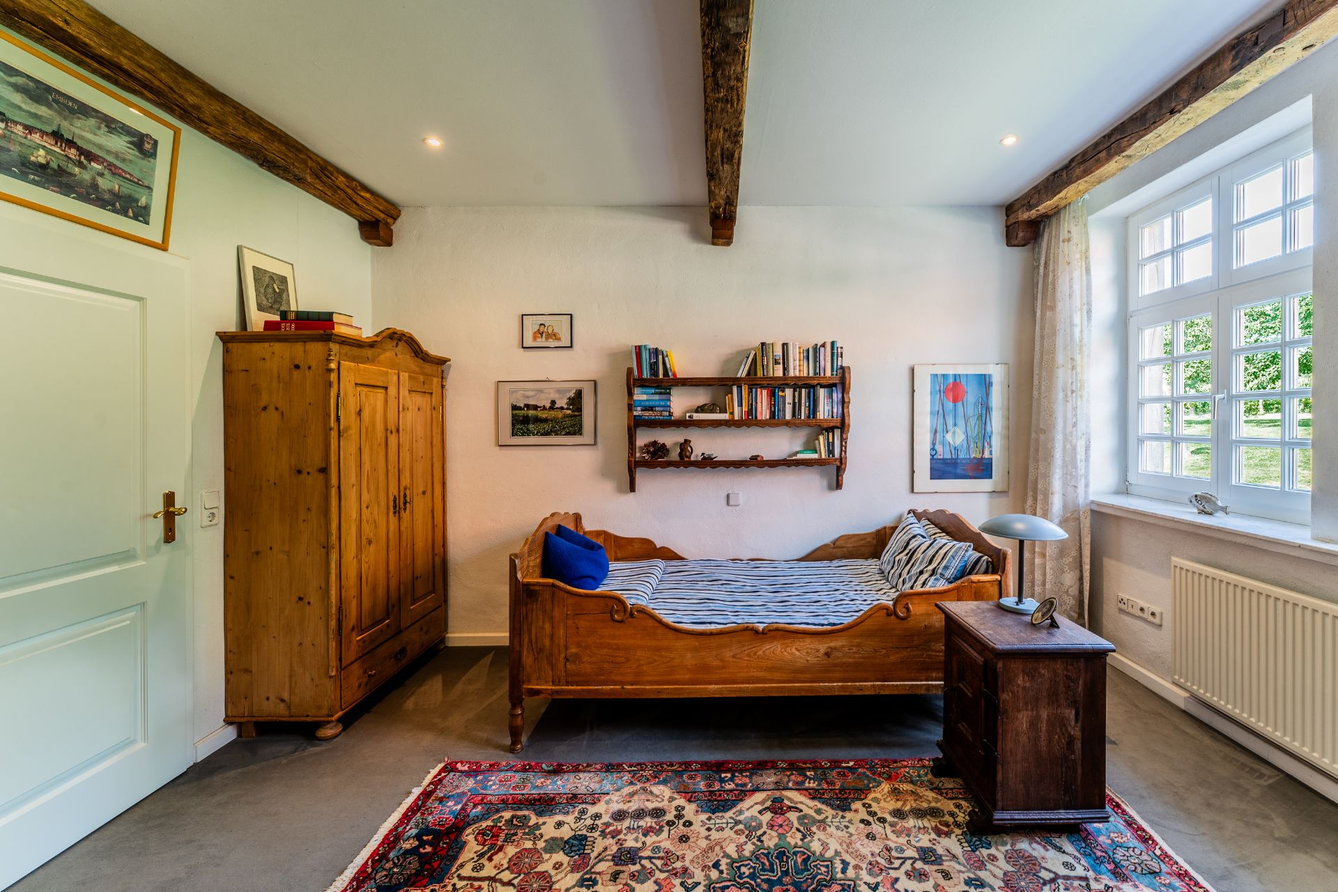 Gemütliches Schlafzimmer mit Holzbett, Teppich, Schrank, Nachttisch und großem Fenster.