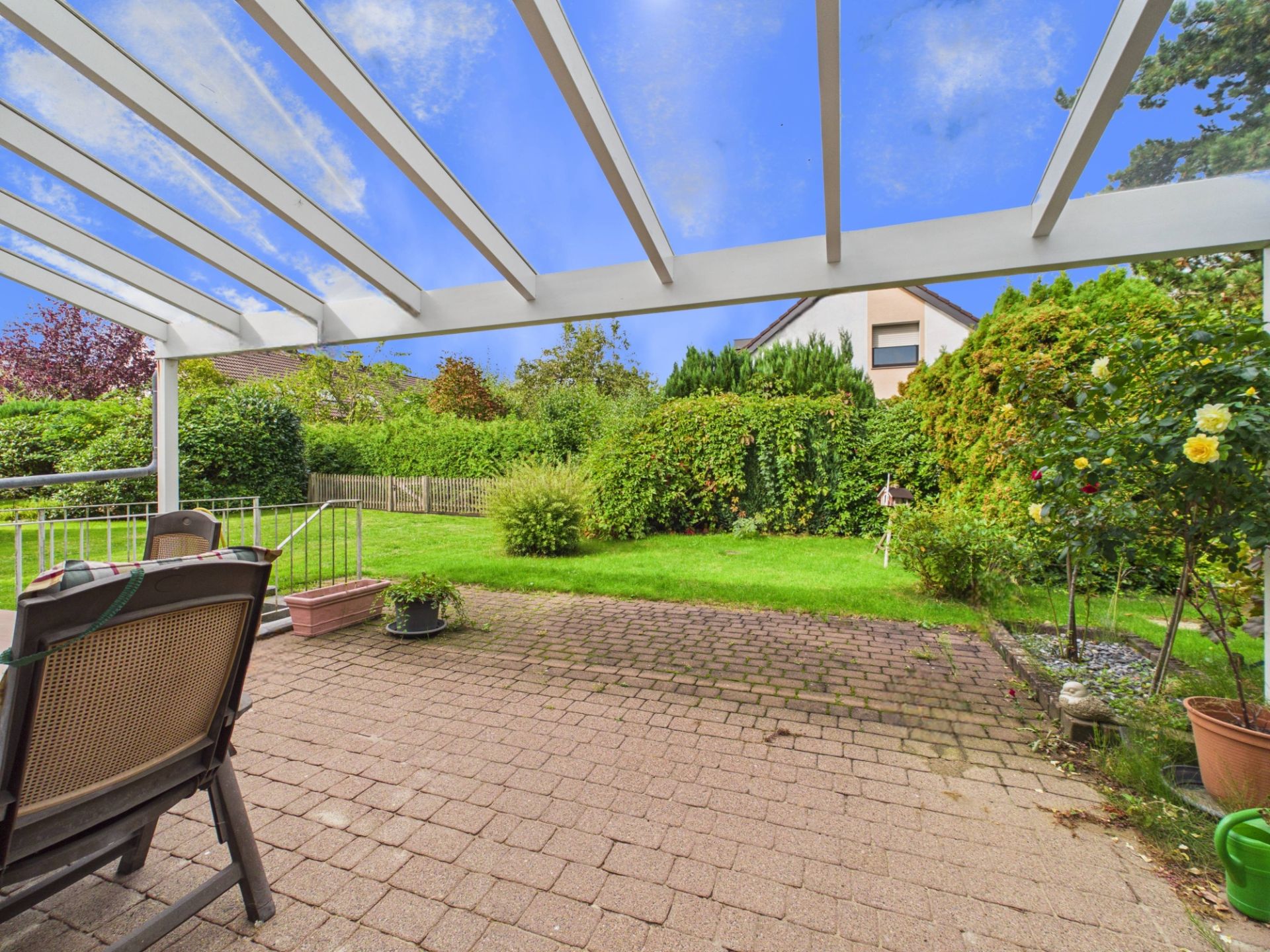 Überdachte Terrasse mit Gartenblick und Gartenmöbeln, umgeben von viel Grün.