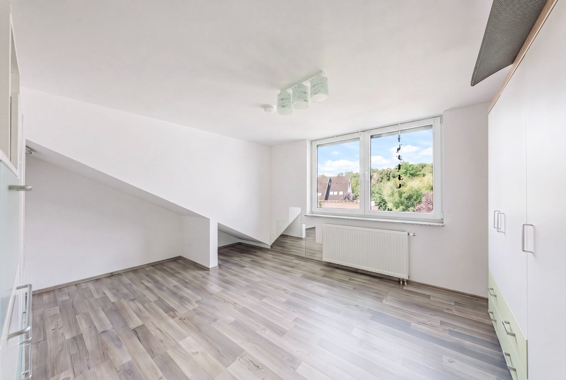 Helles Zimmer mit schräger Decke, großem Fenster und Holzfußboden.
