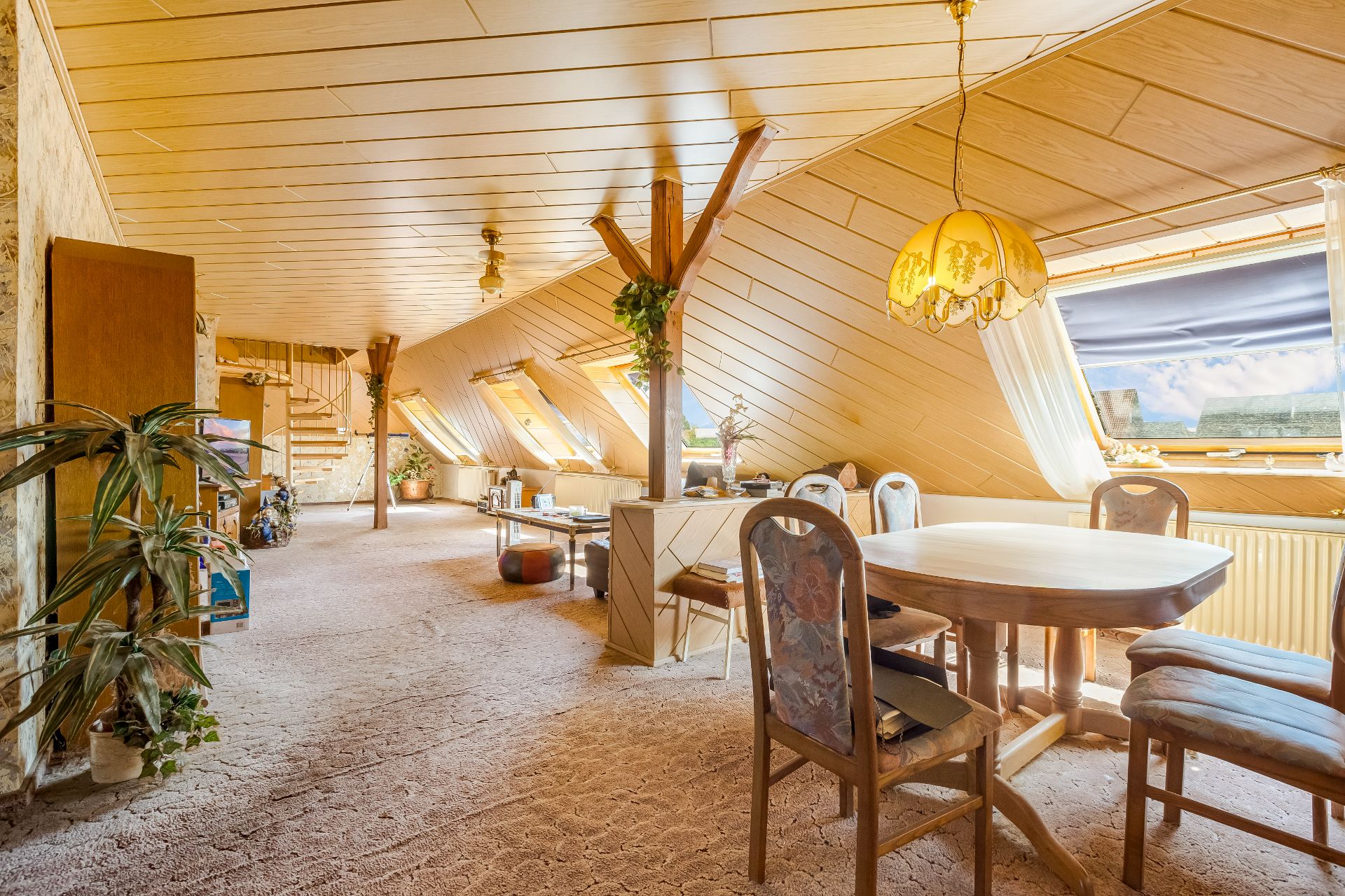 Helles Dachgeschosszimmer mit Holztäfelung, Esstisch und mehreren Fenstern.