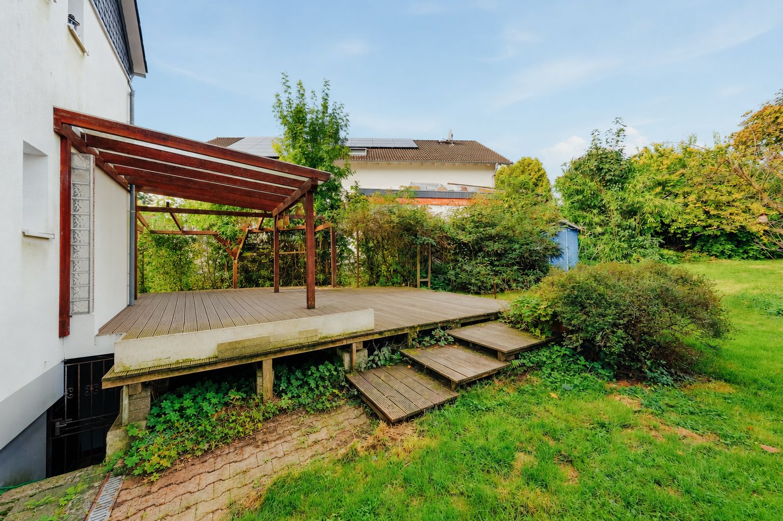 Holzterrasse mit Überdachung und Stufen im Garten eines Wohnhauses.