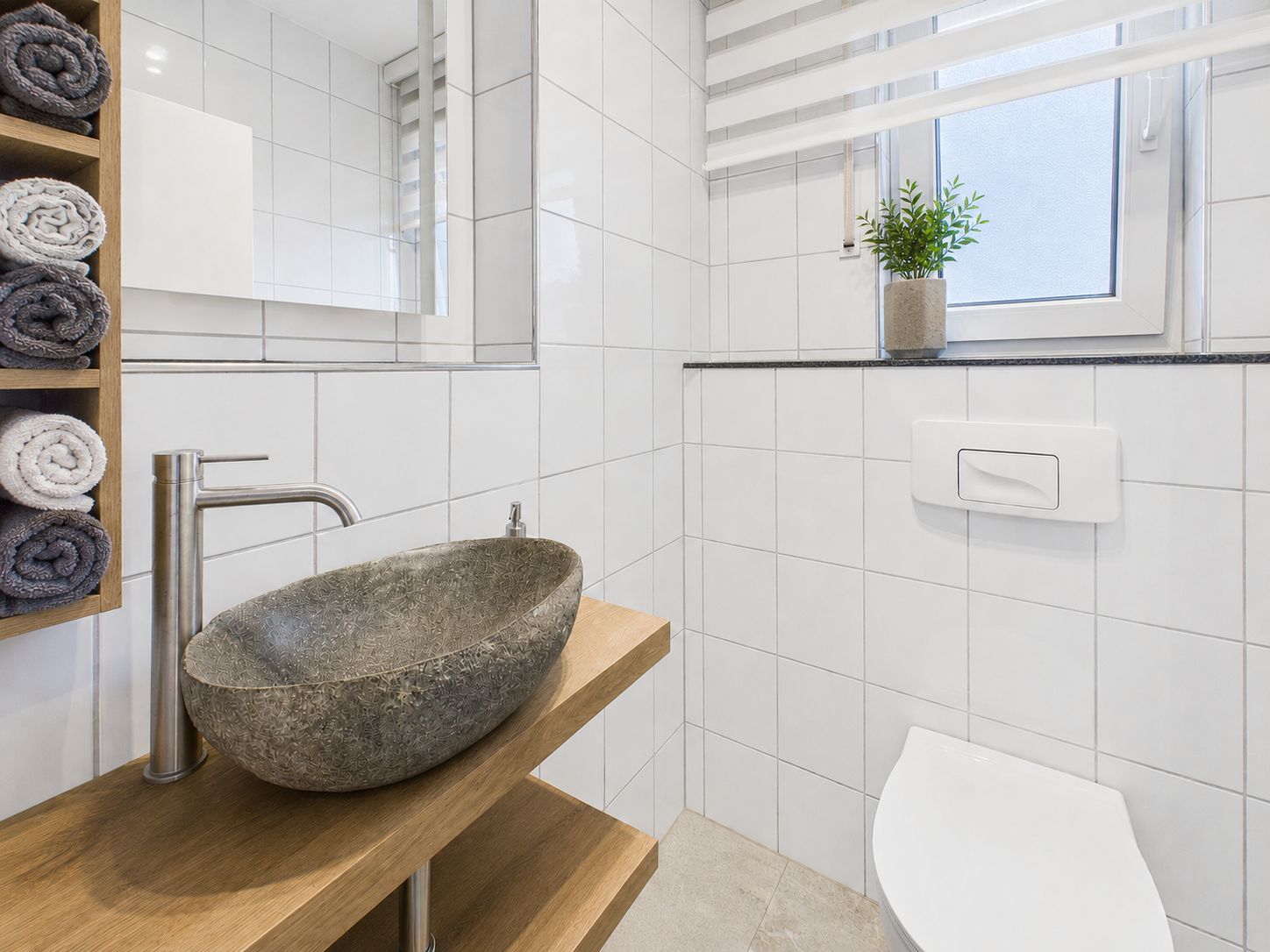 Modernes Badezimmer mit Steinwaschbecken, offenem Regal und Fenster mit Pflanze.