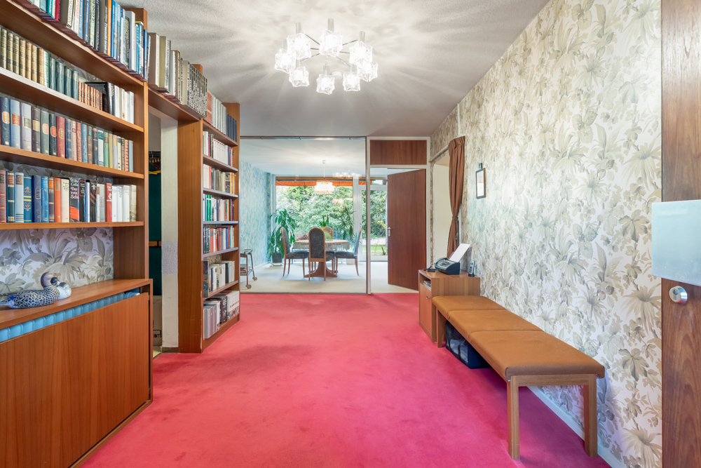 Flur mit rotem Teppich, Bücherregalen, Bank und Blick in ein Esszimmer mit großen Fenstern.