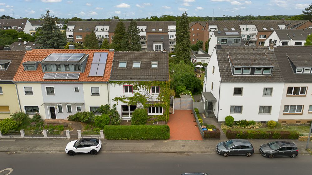 Mehrere Reihenhäuser mit Vorgärten und parkenden Autos auf der Straße, fotografiert aus der Luft.