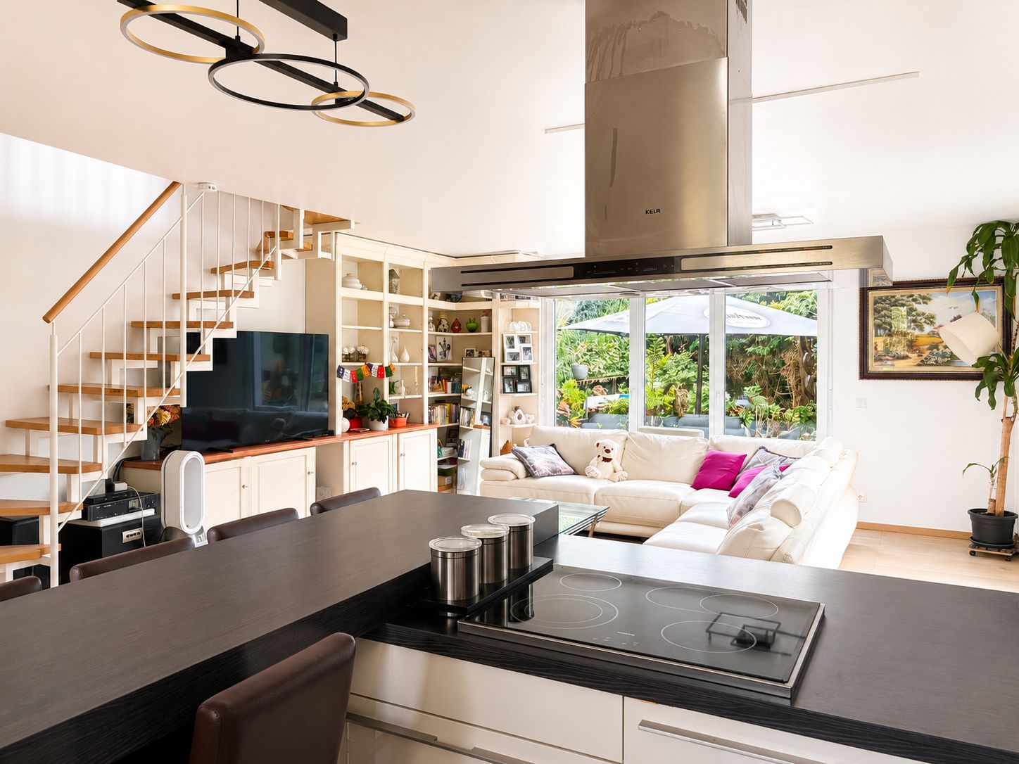 Moderne offene Küche mit Wohnzimmer, Treppe, Sofaecke und großen Fenstern zum Garten.
