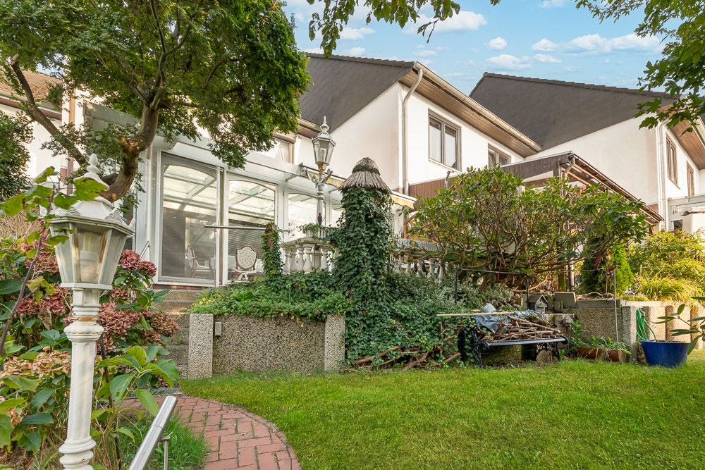Garten mit Rasen, Bäumen, Rankpflanzen und Glaswintergarten eines Wohnhauses.