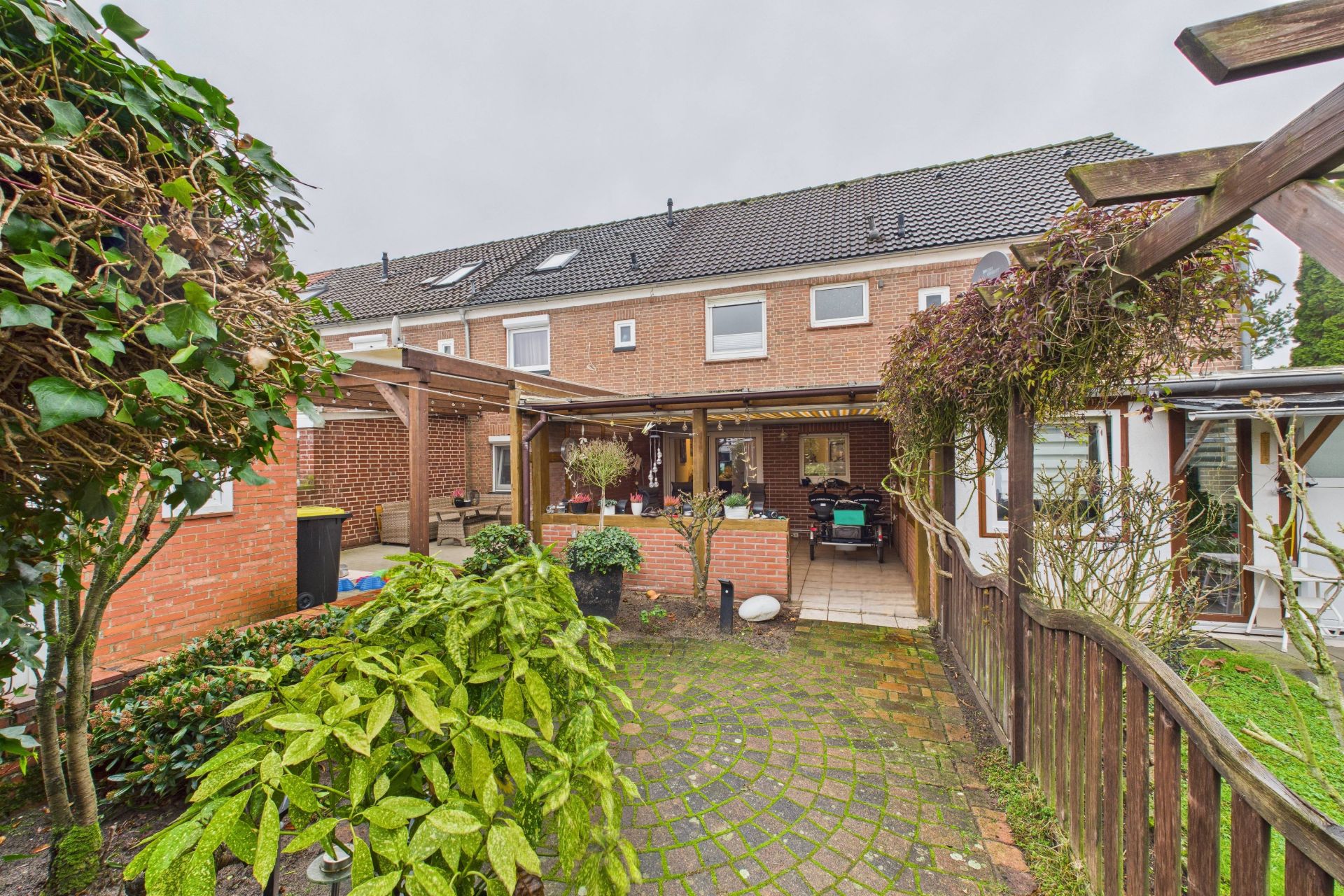 Garten mit überdachter Terrasse und Blick auf ein zweistöckiges Backsteinhaus.