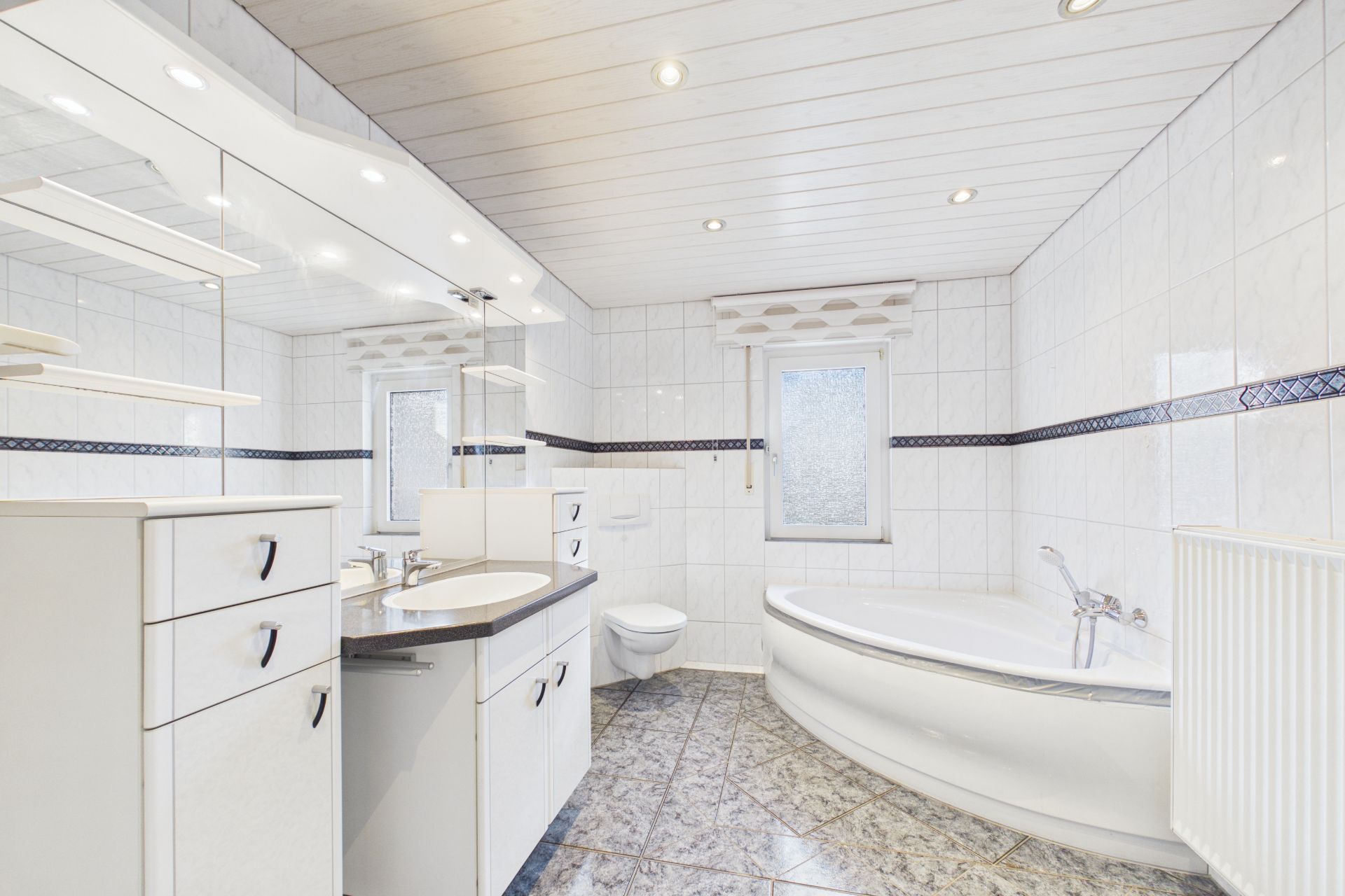 Helles Badezimmer mit Eckbadewanne, großem Spiegel, Waschbecken und Toilette.