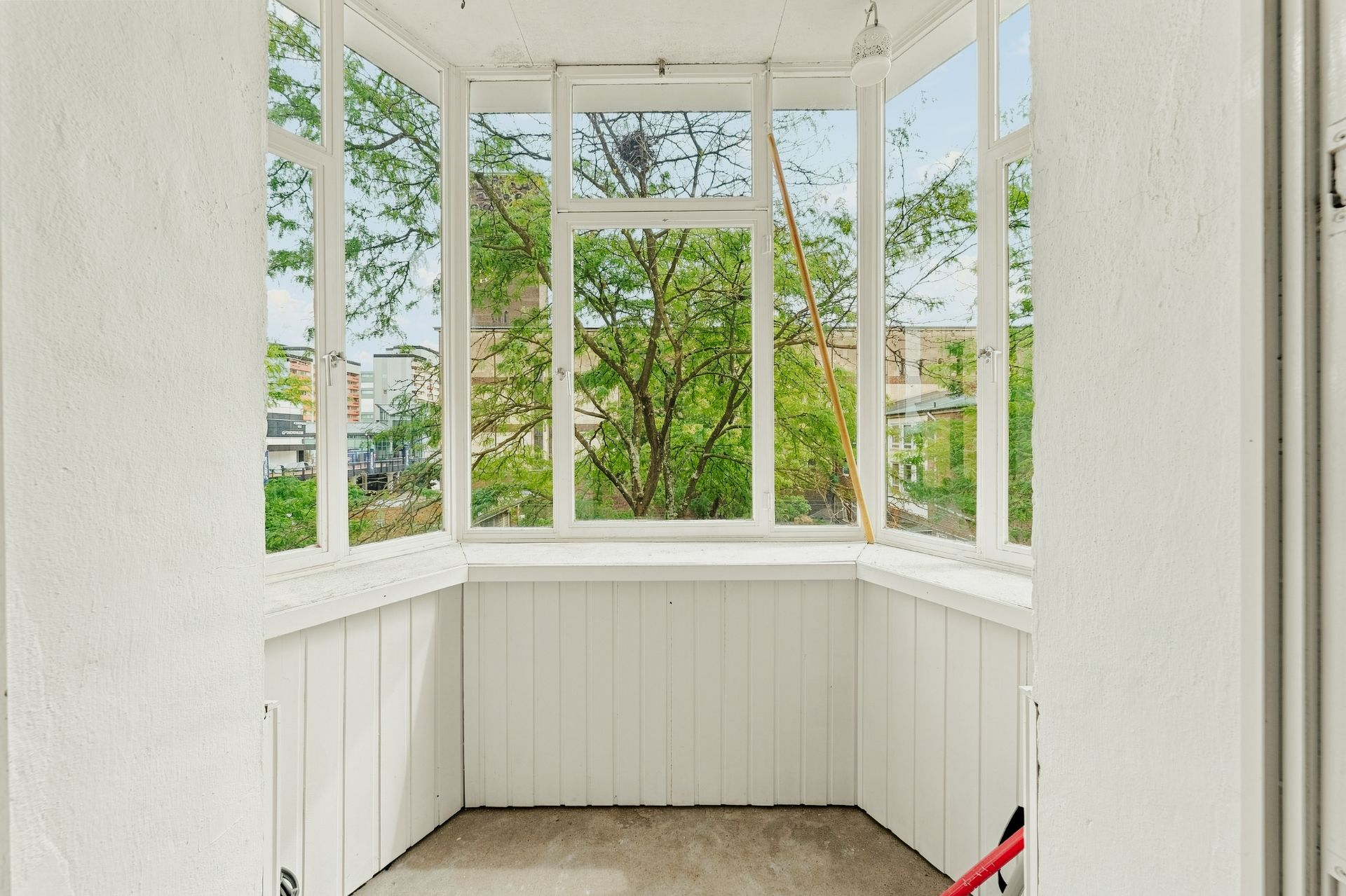 Heller Balkon mit weißen Wänden und großen Fenstern, Blick auf grüne Bäume.