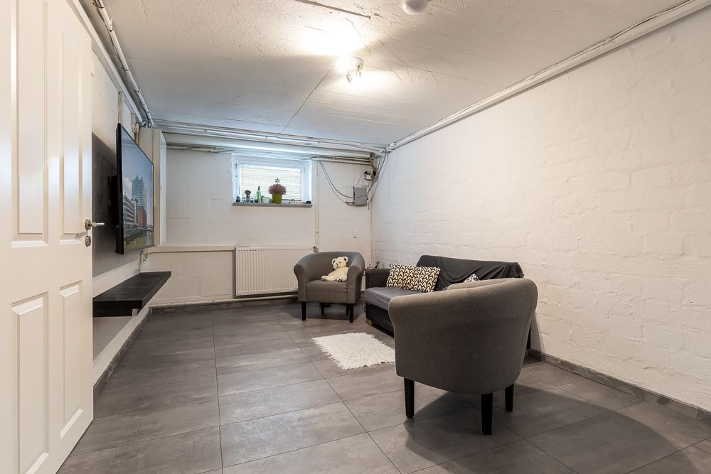 Kleiner Wohnraum mit zwei Sesseln, einem Sofa, einem Teppich und einem Fernsehgerät an der Wand.