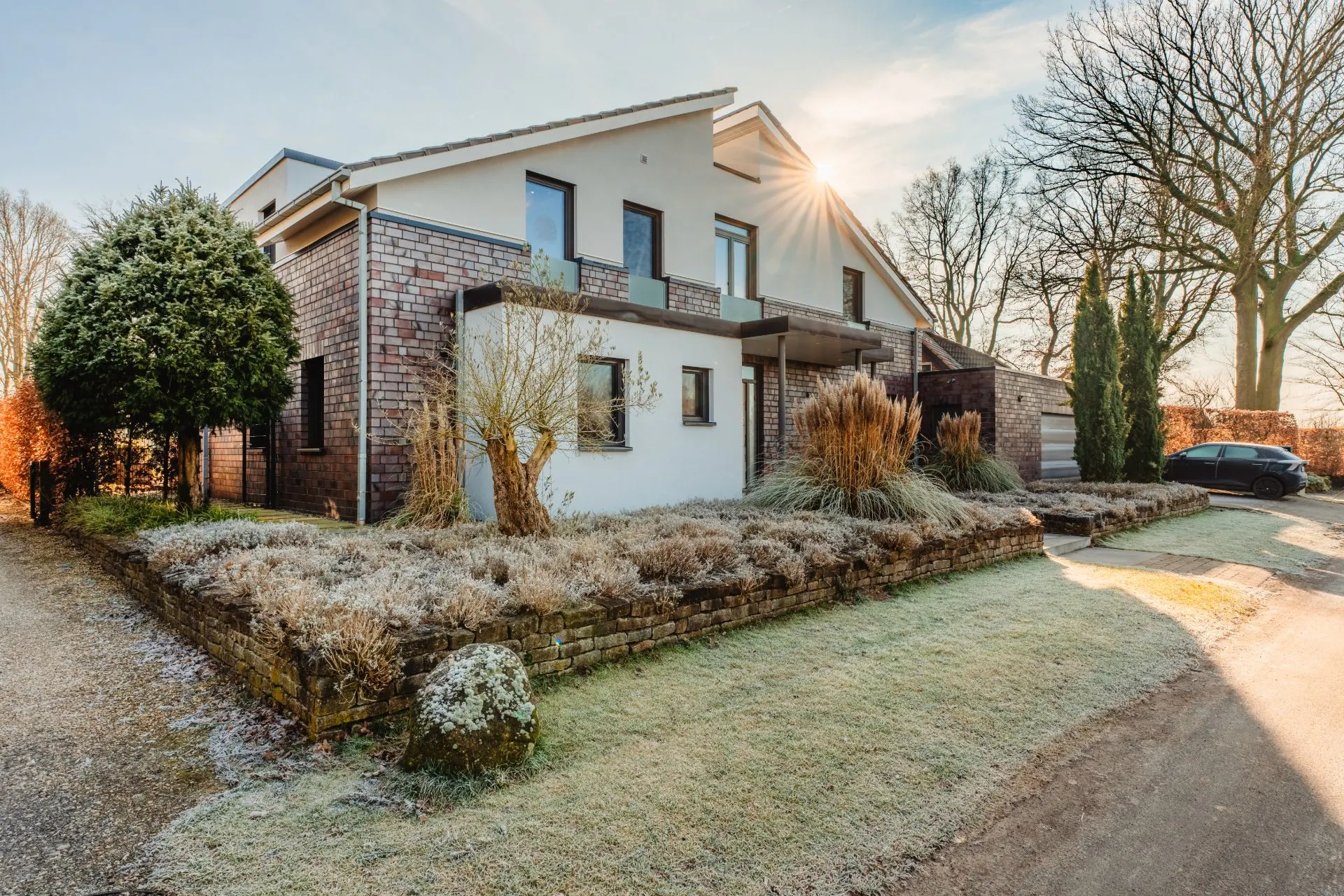 Modernes Wohnhaus mit Garten, Kiesweg und geparktem Auto, Winterstimmung mit leichtem Frost.