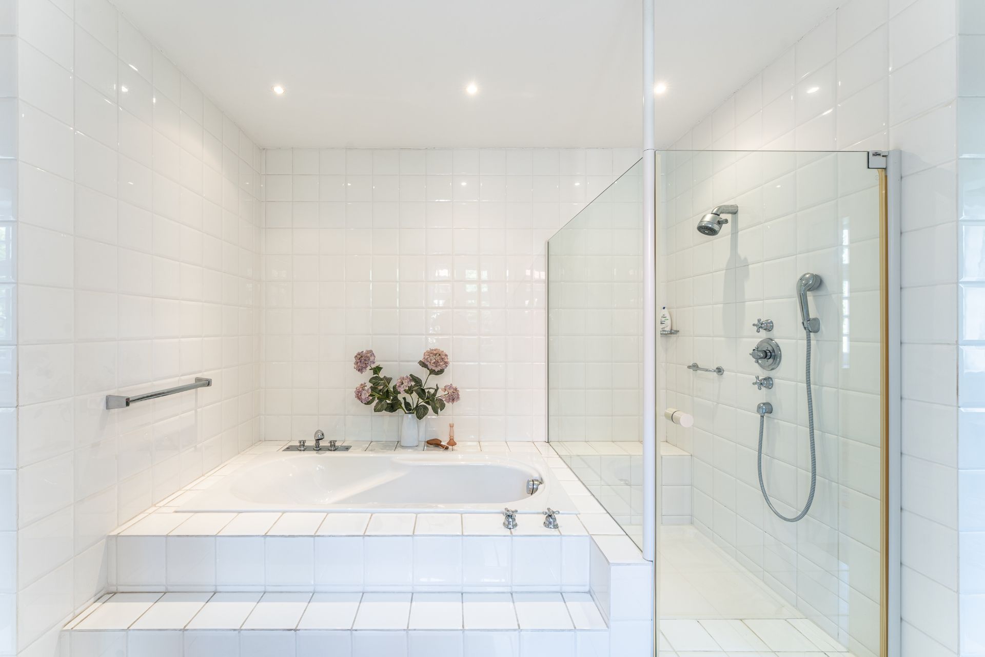 Helles Badezimmer mit eingelassener Badewanne, Glasdusche und weißen Fliesen.