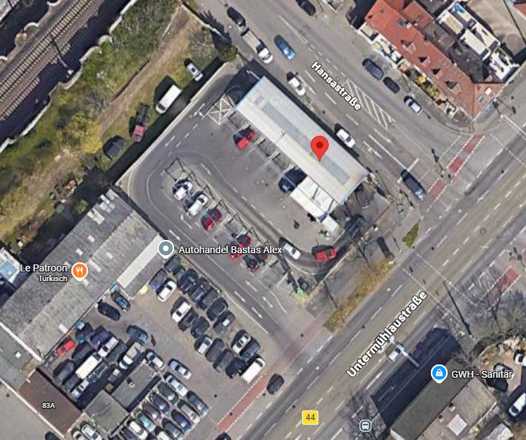 Luftbild von einem Parkplatz mit mehreren Autos und einem langgestreckten Gebäude an einer Straßenecke.