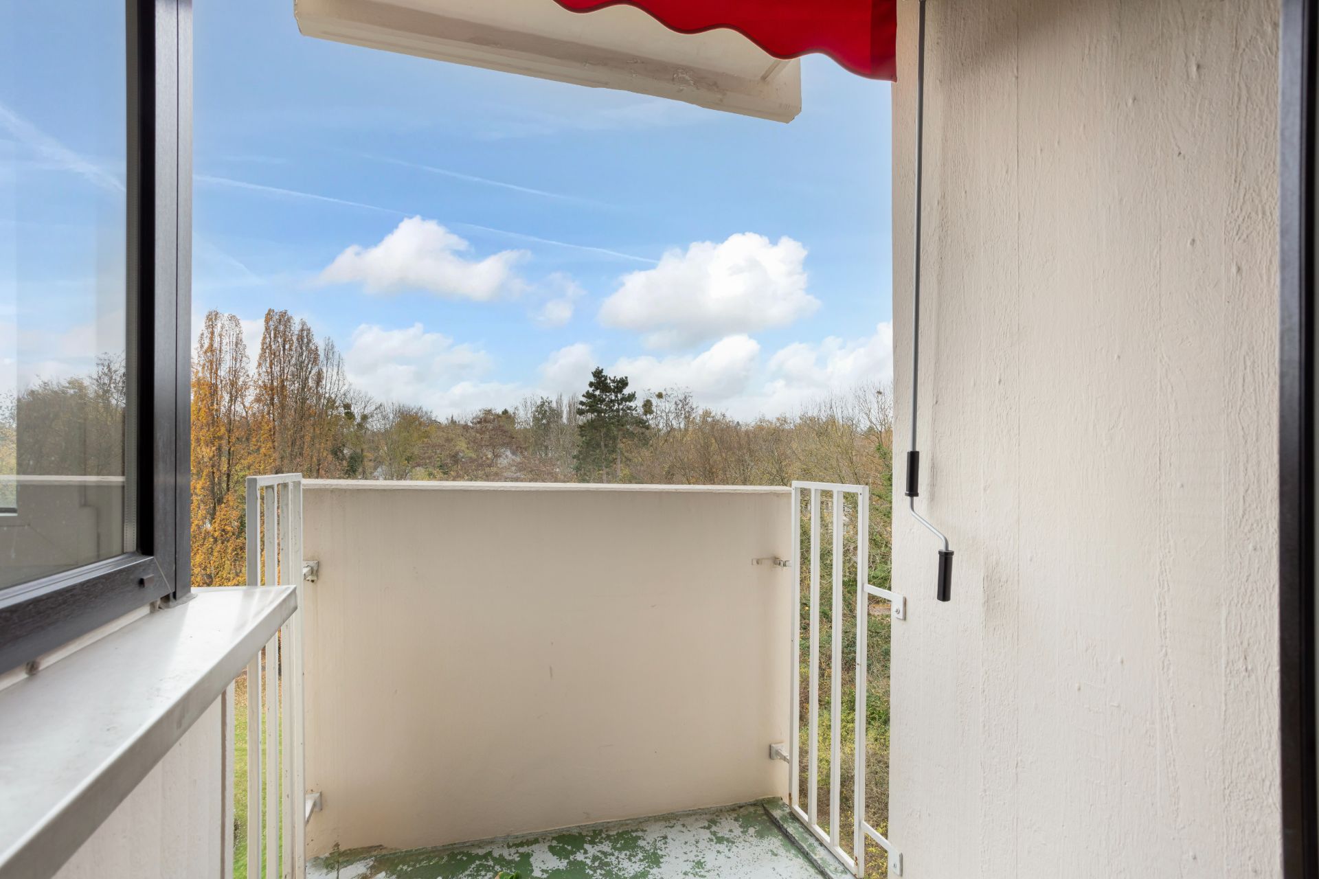 Kleiner Balkon mit Geländer und Blick ins Grüne, Teil einer Markise oben sichtbar.