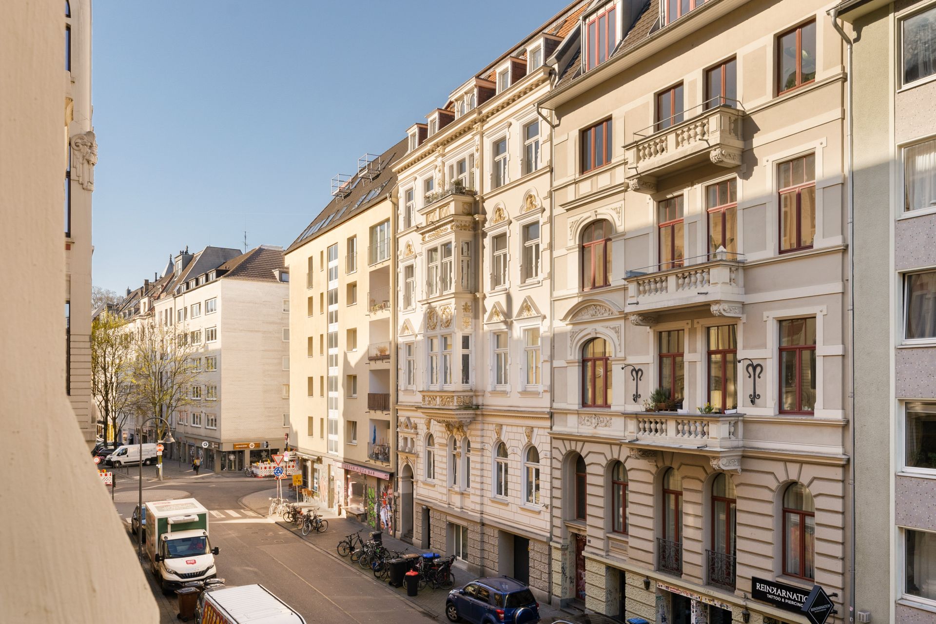Blick auf eine ruhige Wohnstraße mit mehrstöckigen Altbauten und geparkten Autos.