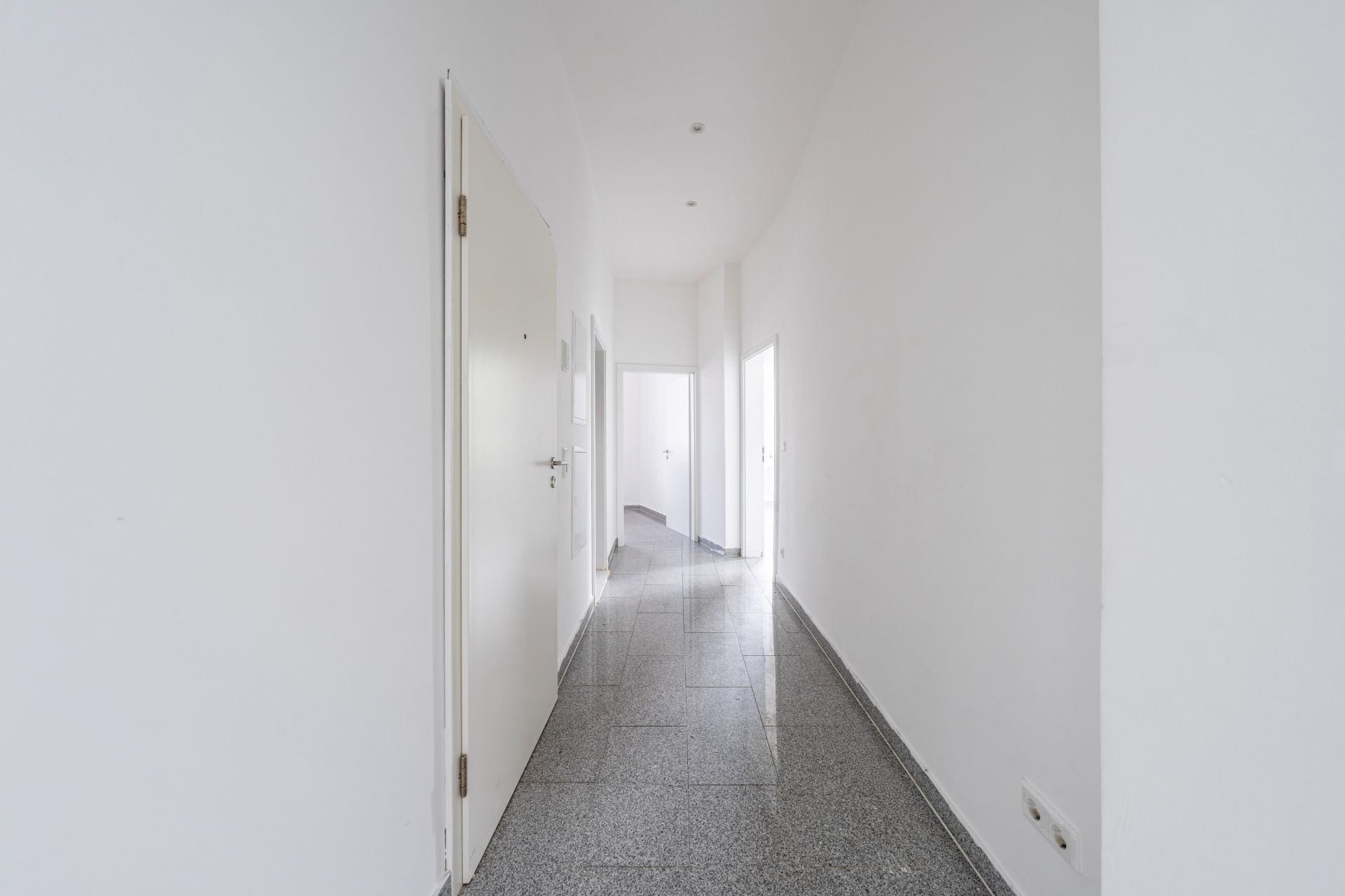 Heller Flur mit grauem Boden und weißen Türen in einer Wohnung.