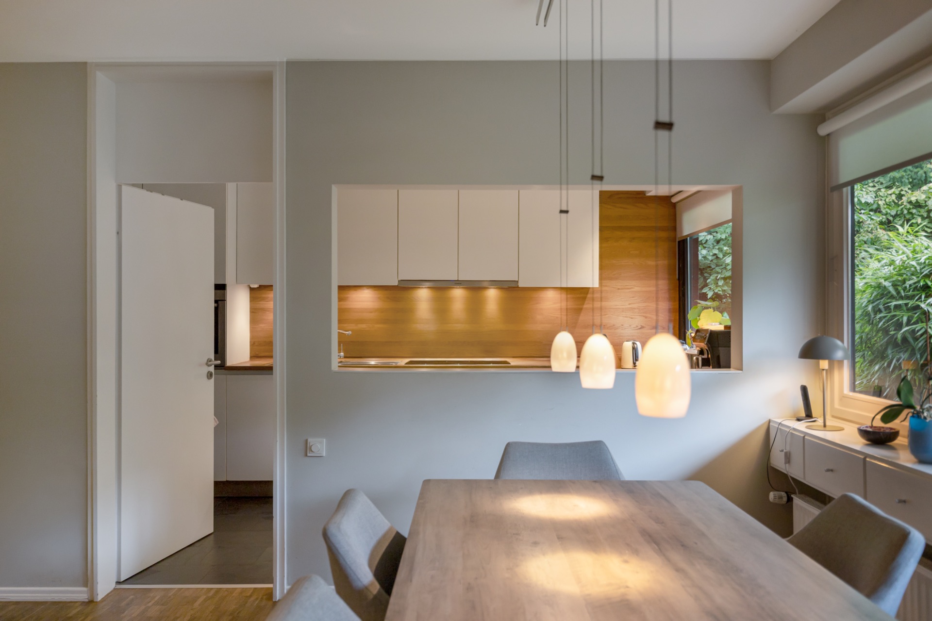 Essbereich mit Holztisch, Stühlen und Blick in eine moderne Küche mit Holzrückwand und Hängelampen.
