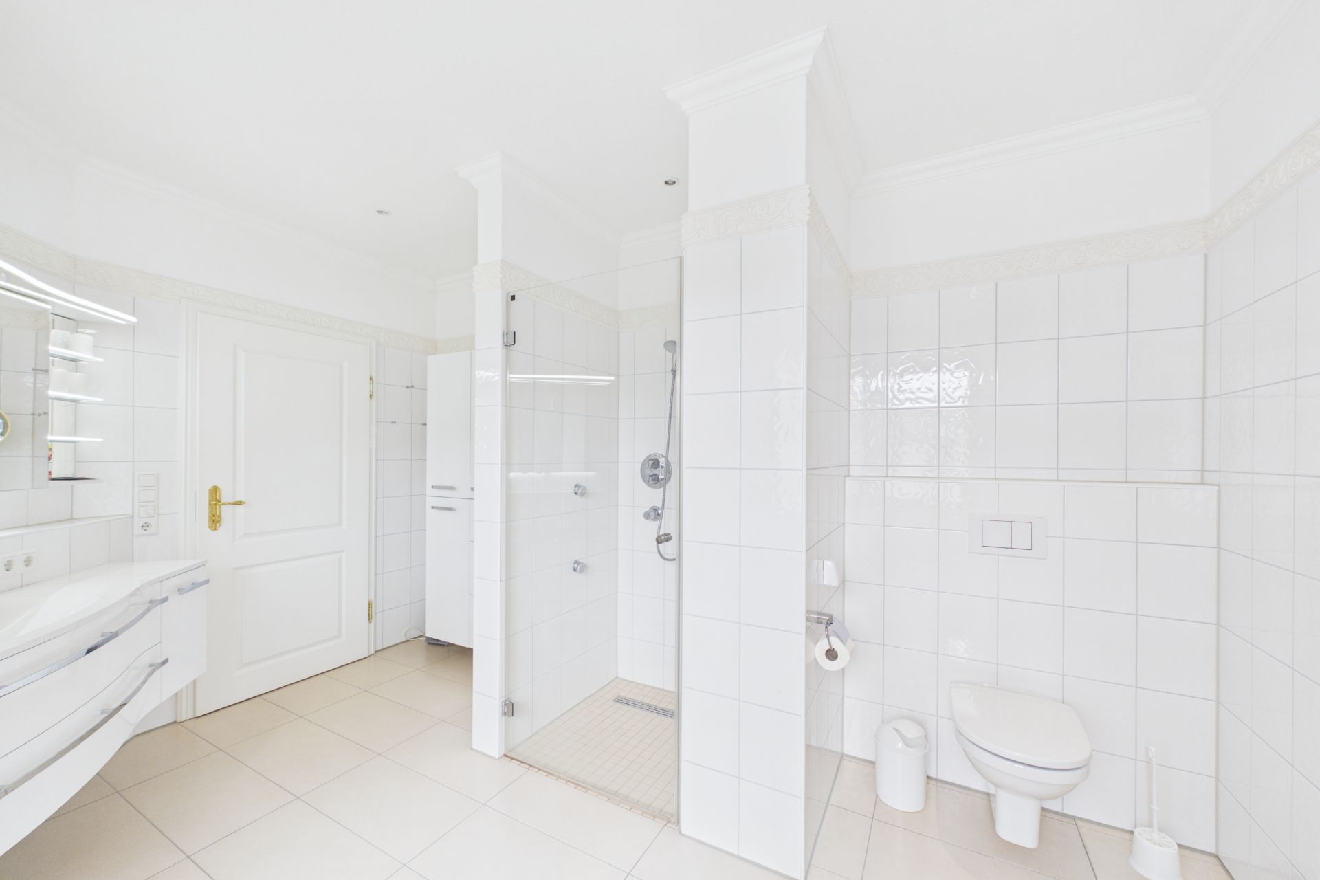 Modernes, helles Badezimmer mit Dusche, WC und Waschbecken, alles mit weißen Fliesen.