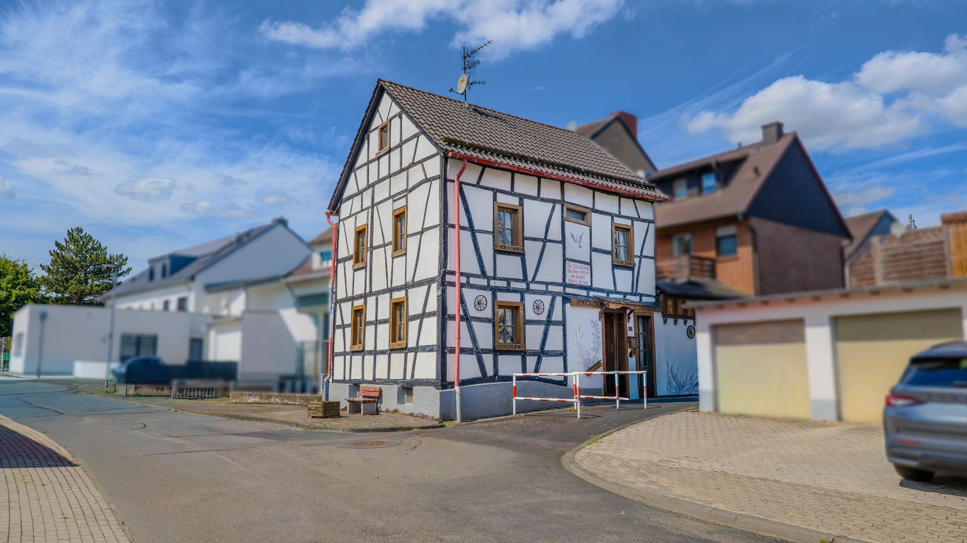 Fachwerkhaus an einer Straßenecke mit Garagen und geparktem Auto daneben.