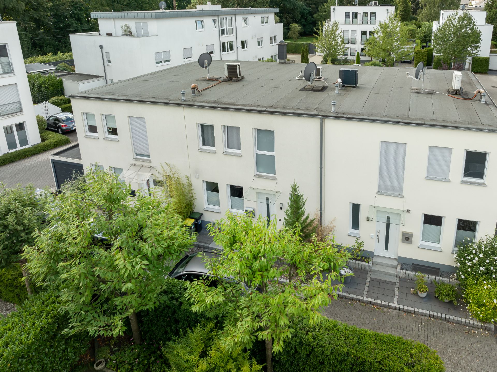 Zwei moderne, weiße Reihenhäuser mit Flachdach und Bäumen im Vordergrund.
