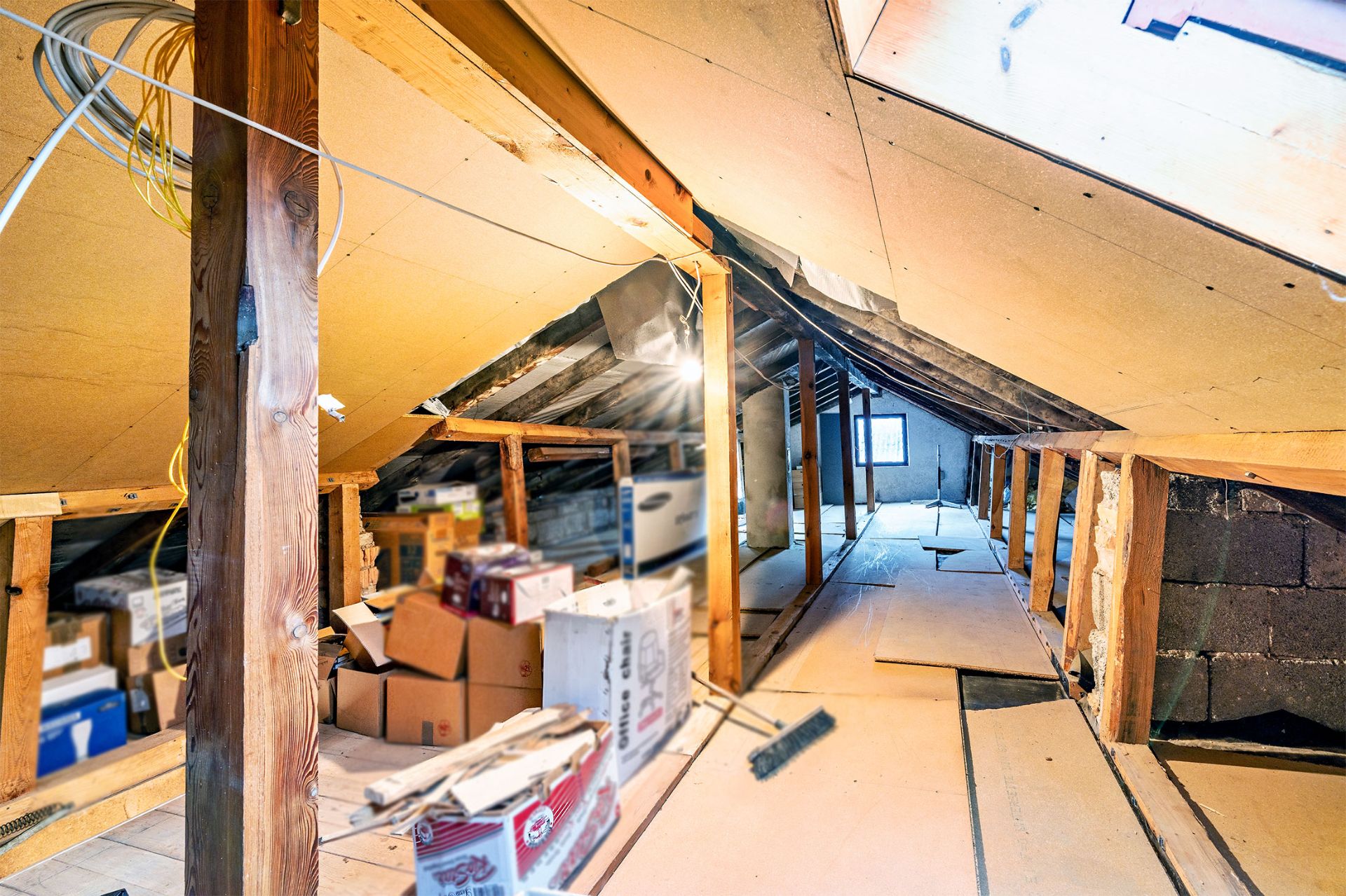 Dachboden mit Holzbalken, Kartons und losem Boden, Tageslicht durch Dachfenster.
