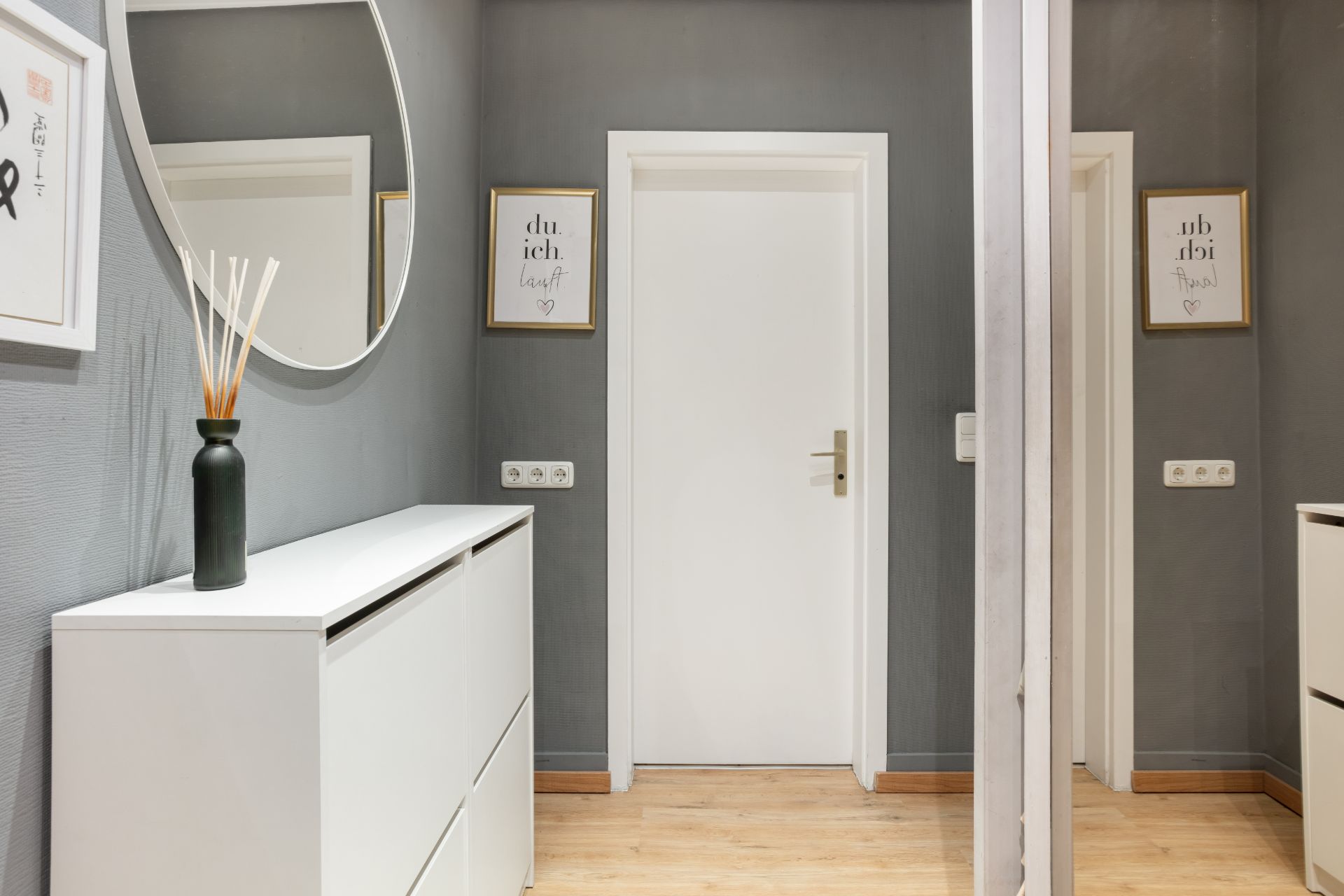 Moderner Flur mit grauen Wänden, weißer Tür, Spiegel und weißem Sideboard mit Vase.