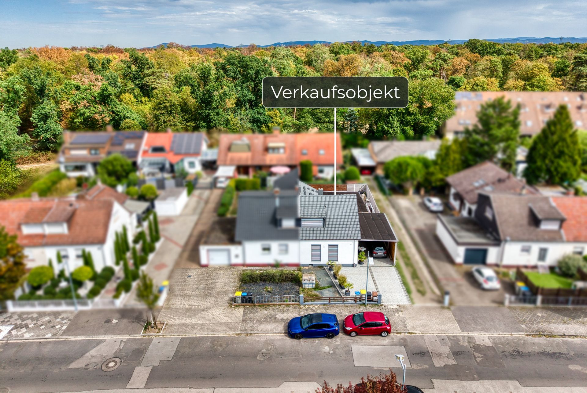 Luftaufnahme eines Einfamilienhauses mit Garten und zwei Autos davor, mit Schild 'Verkaufsobjekt'.