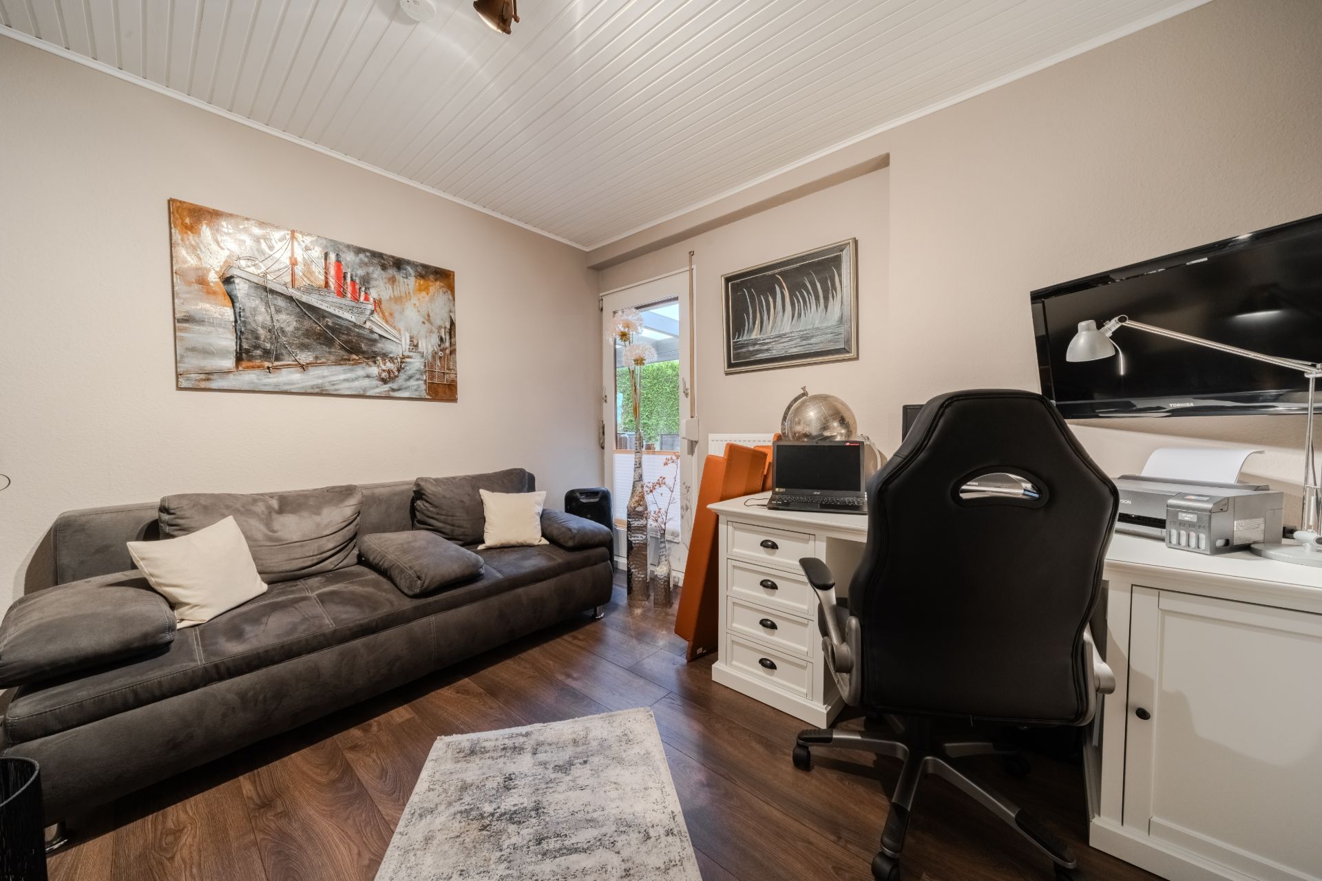 Modernes Wohnzimmer mit Sofa, Schreibtisch, Stuhl und Wandbildern.