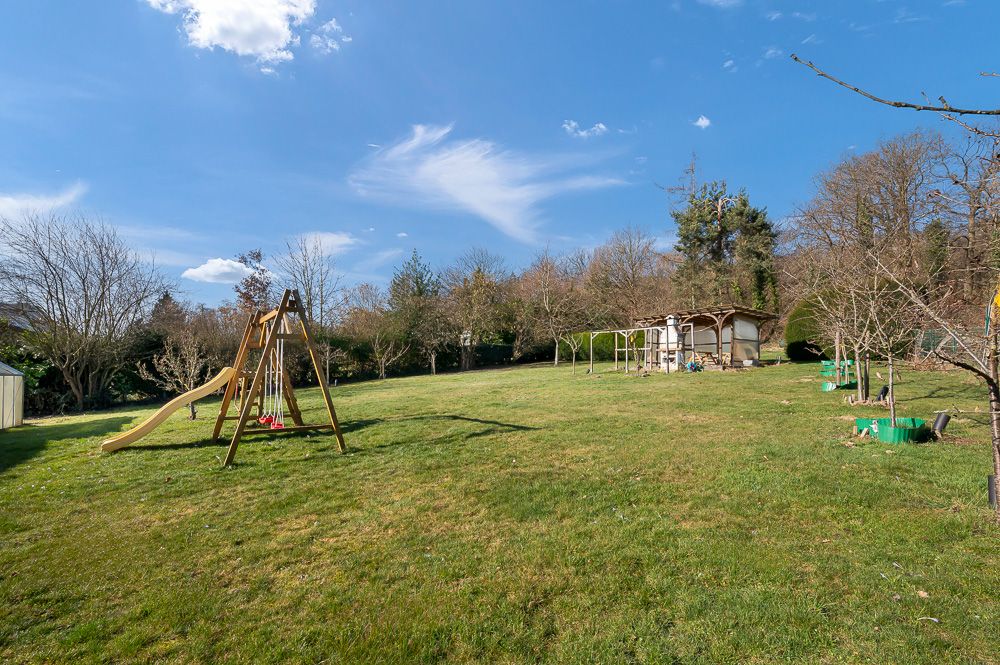 Großer Garten mit Rasenfläche, Spielgerüst und Bäumen unter blauem Himmel.
