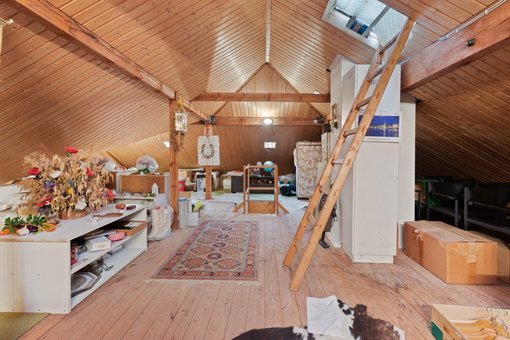 Dachboden mit Holzdecke, Leiter, Teppich und Regalen mit verschiedenen Gegenständen.