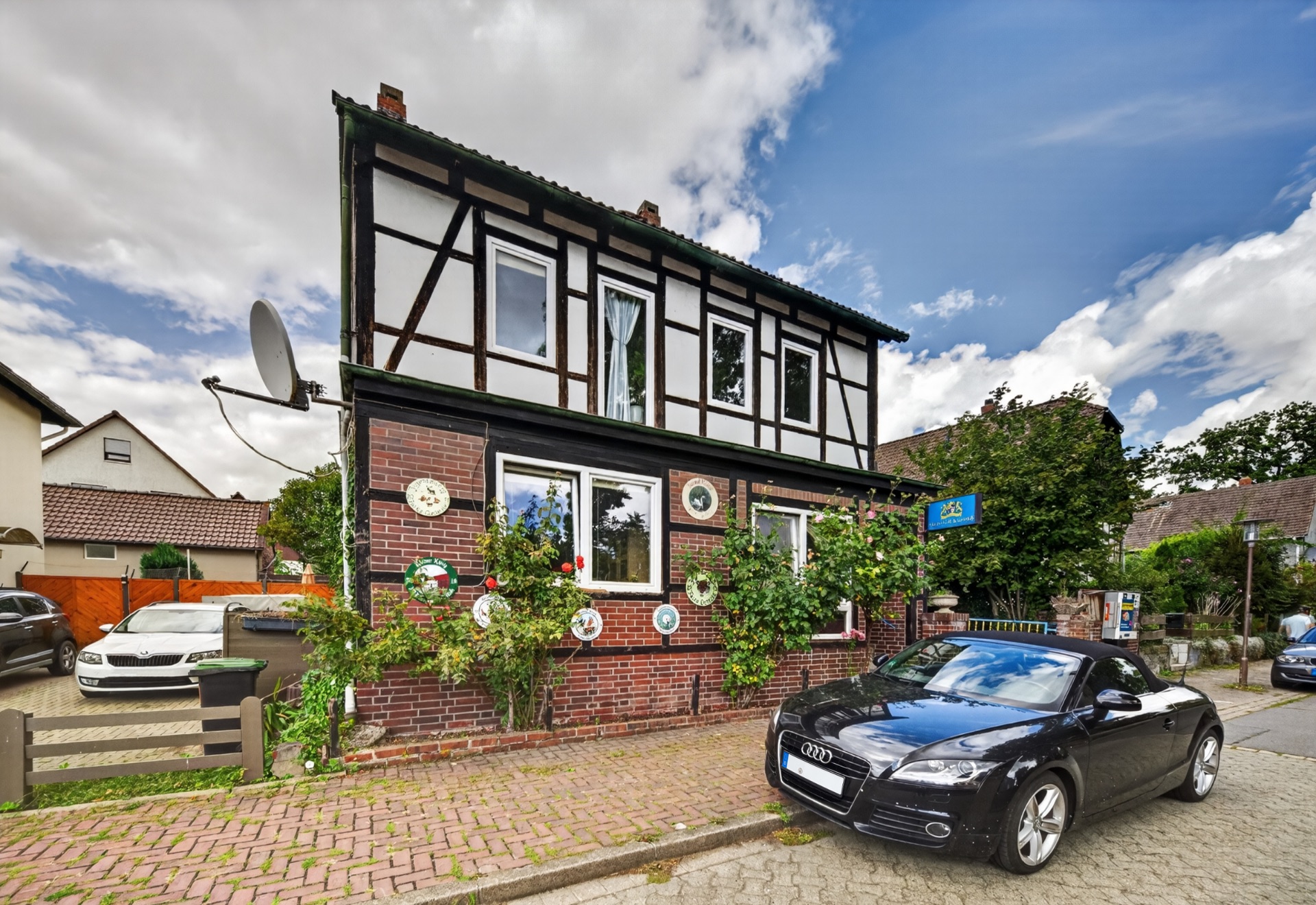 Fachwerkhaus mit roten Ziegeln, bewachsener Fassade und geparktem schwarzen Cabrio davor.