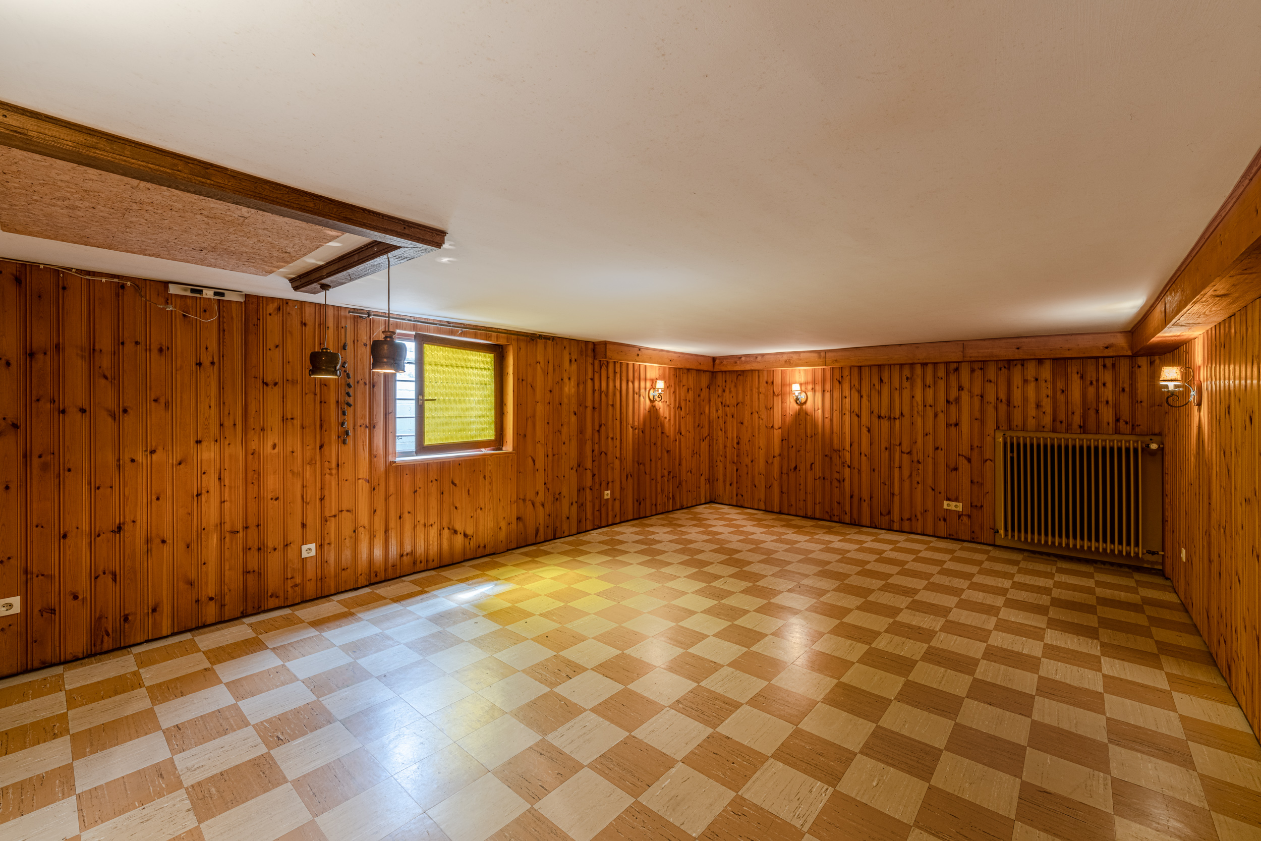 Leerer Raum mit Holzvertäfelung, kariertem Boden, Fenster und Heizkörper.