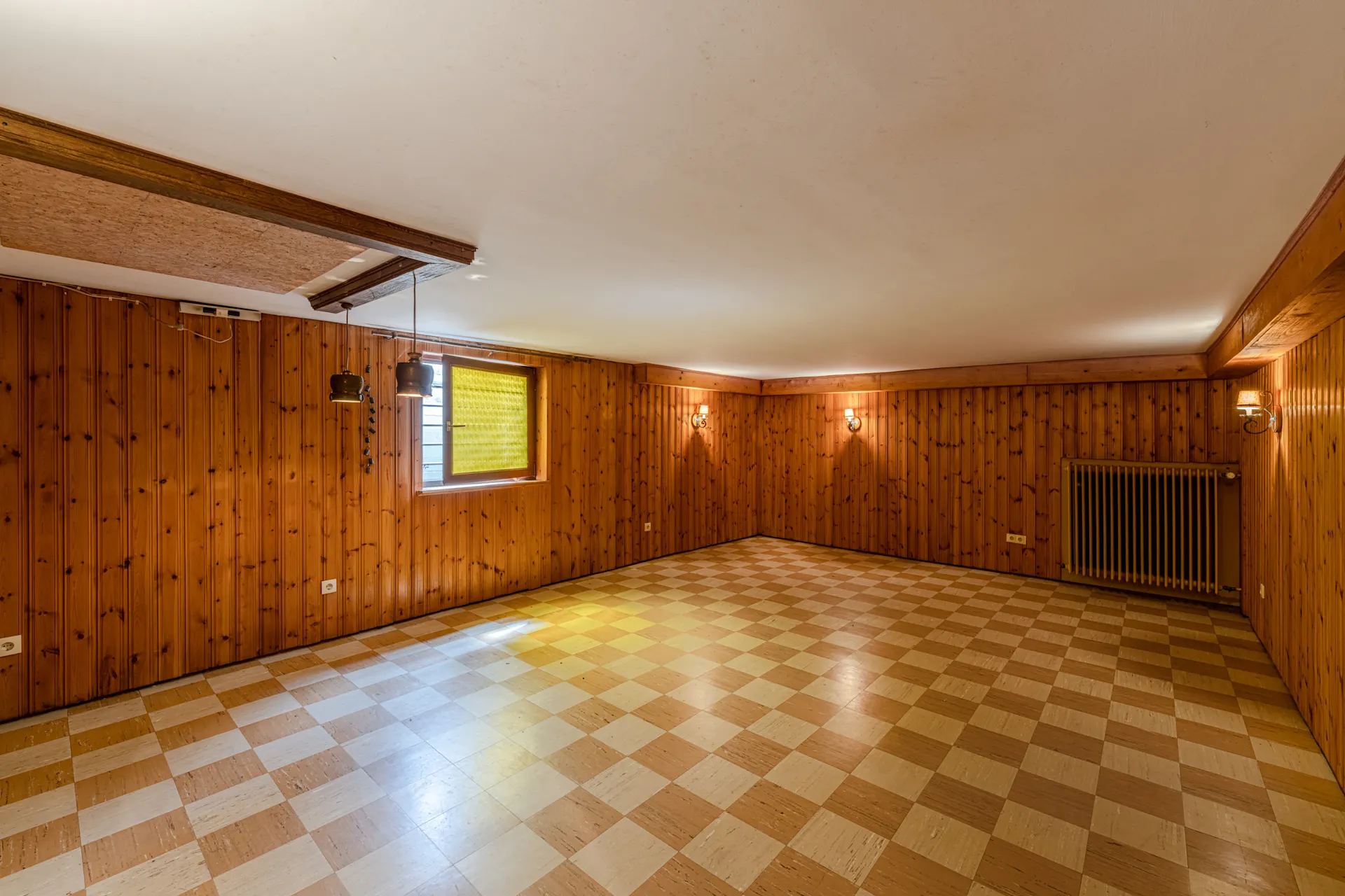 Leerer Raum mit Holzvertäfelung, kariertem Boden, Fenster und Heizkörper.