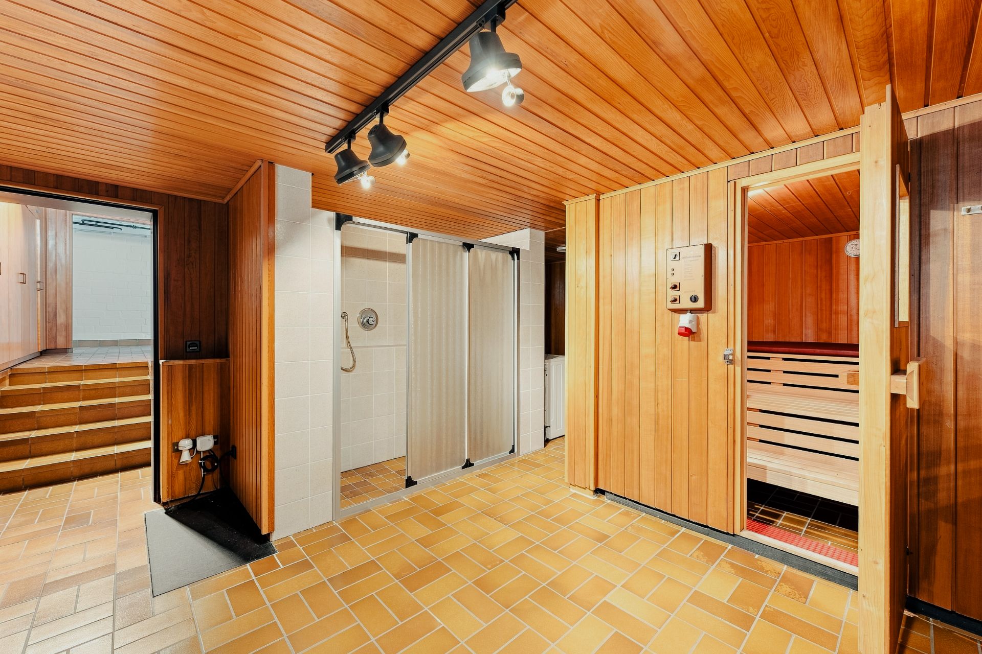 Raum mit Holzwänden, Sauna, gefliestem Boden und zwei offenen Duschkabinen.