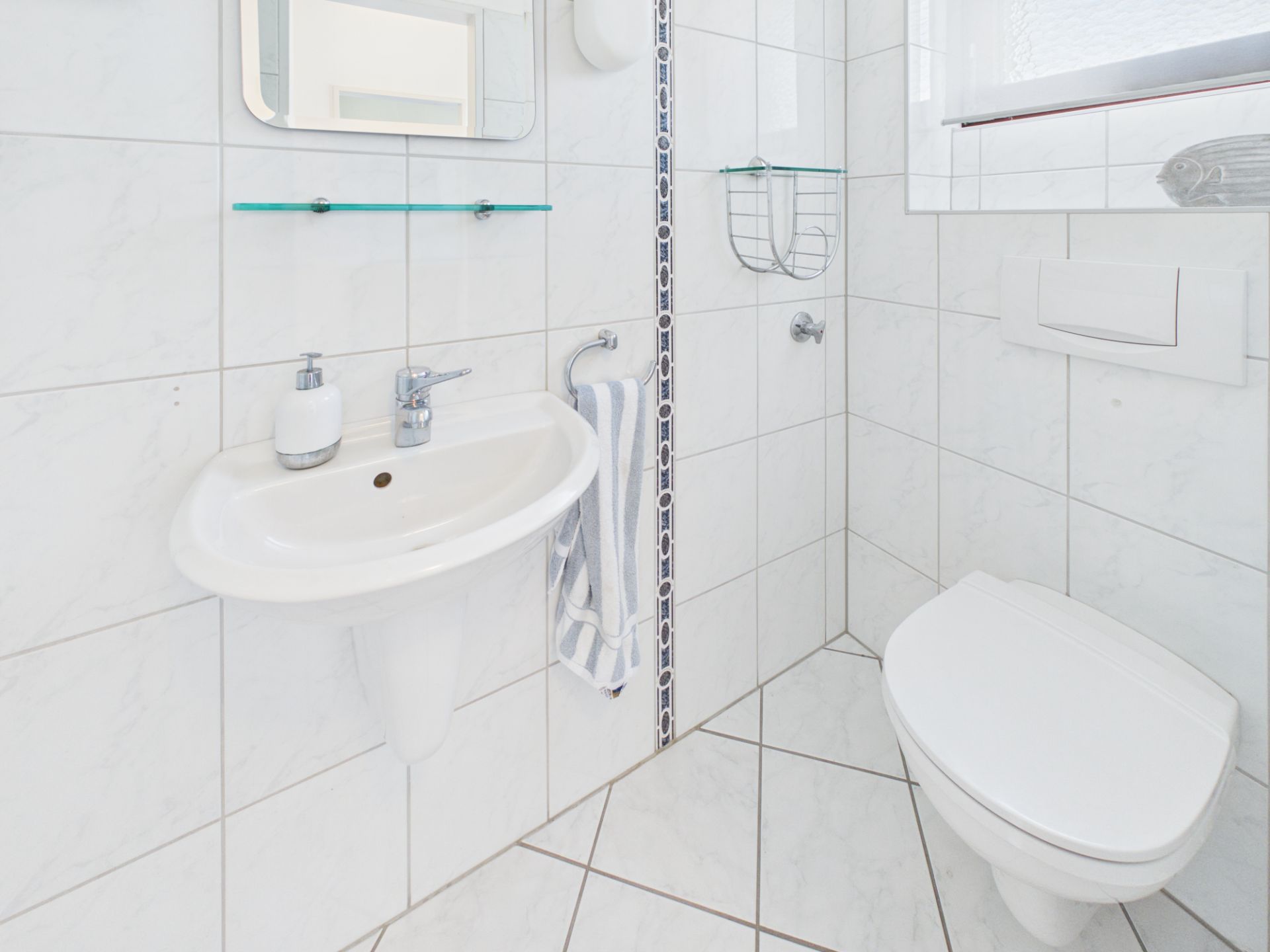 Modernes, weiß gefliestes Badezimmer mit Waschbecken, Spiegel und Toilette.