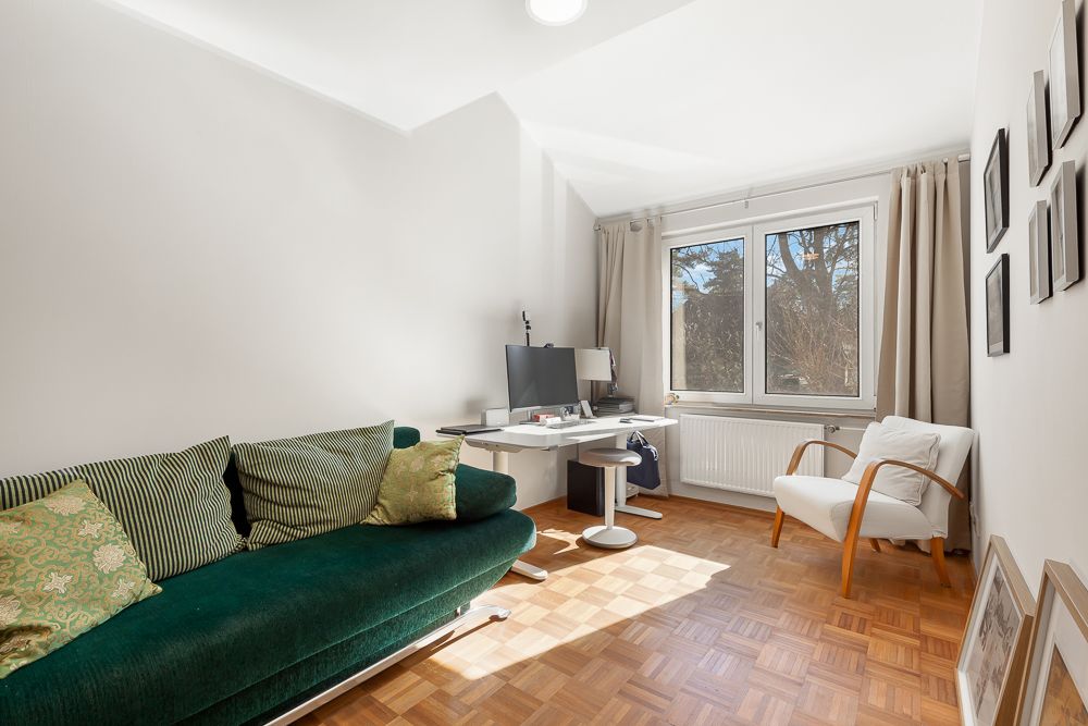 Helles Zimmer mit grünem Sofa, Schreibtisch, Stuhl und Fenster mit Vorhängen.