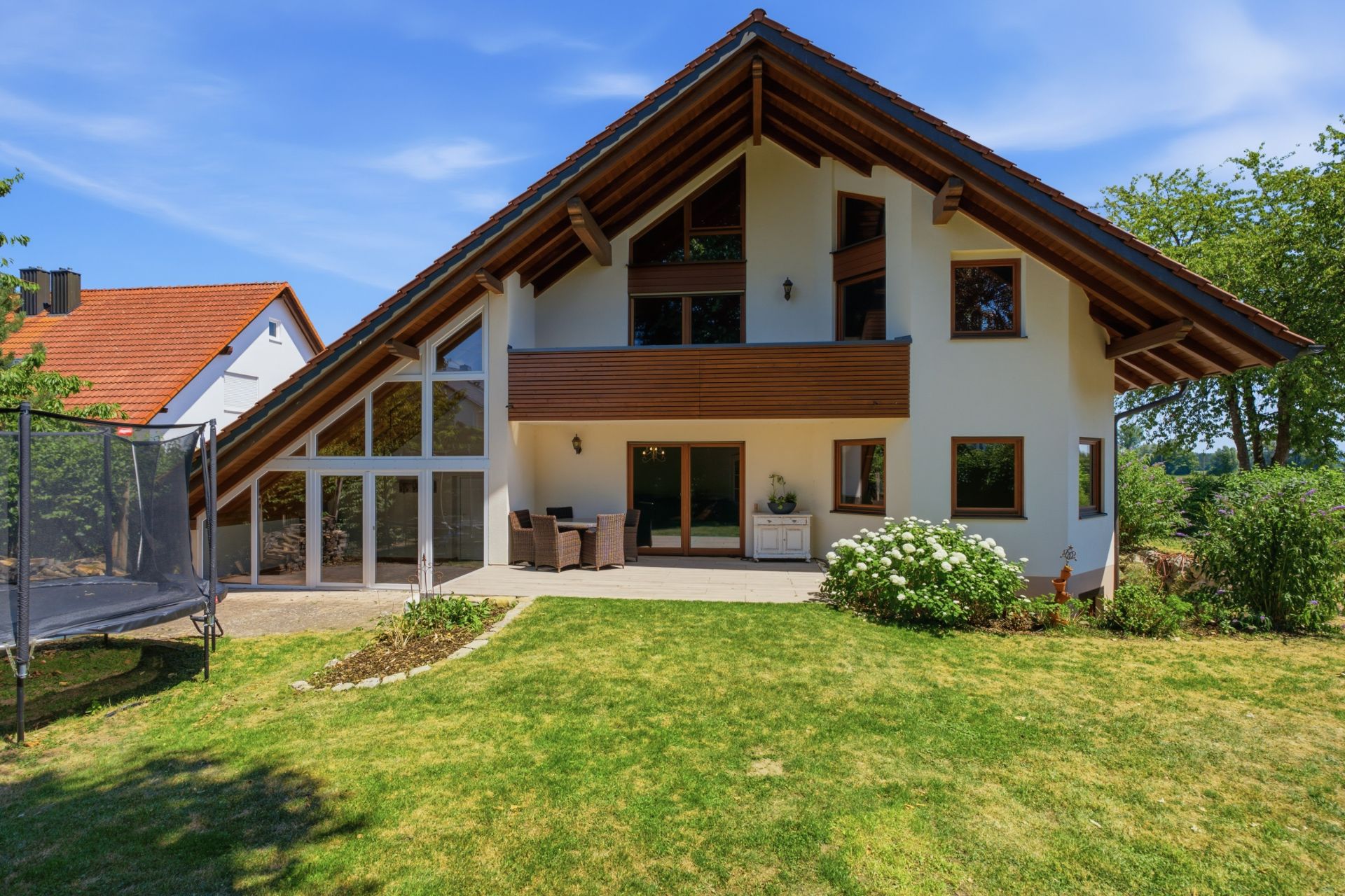 Modernes Haus mit Satteldach, Terrasse und Garten, links steht ein Trampolin.