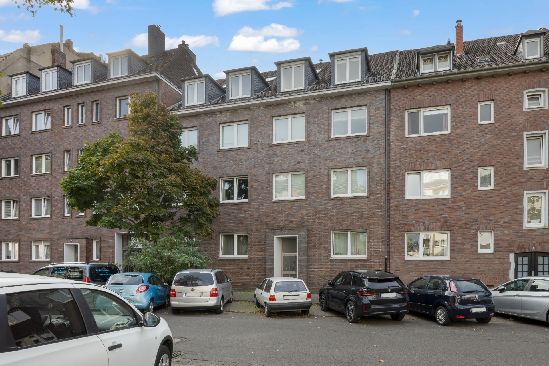Mehrfamilienhaus aus rotem Backstein mit mehreren geparkten Autos davor.