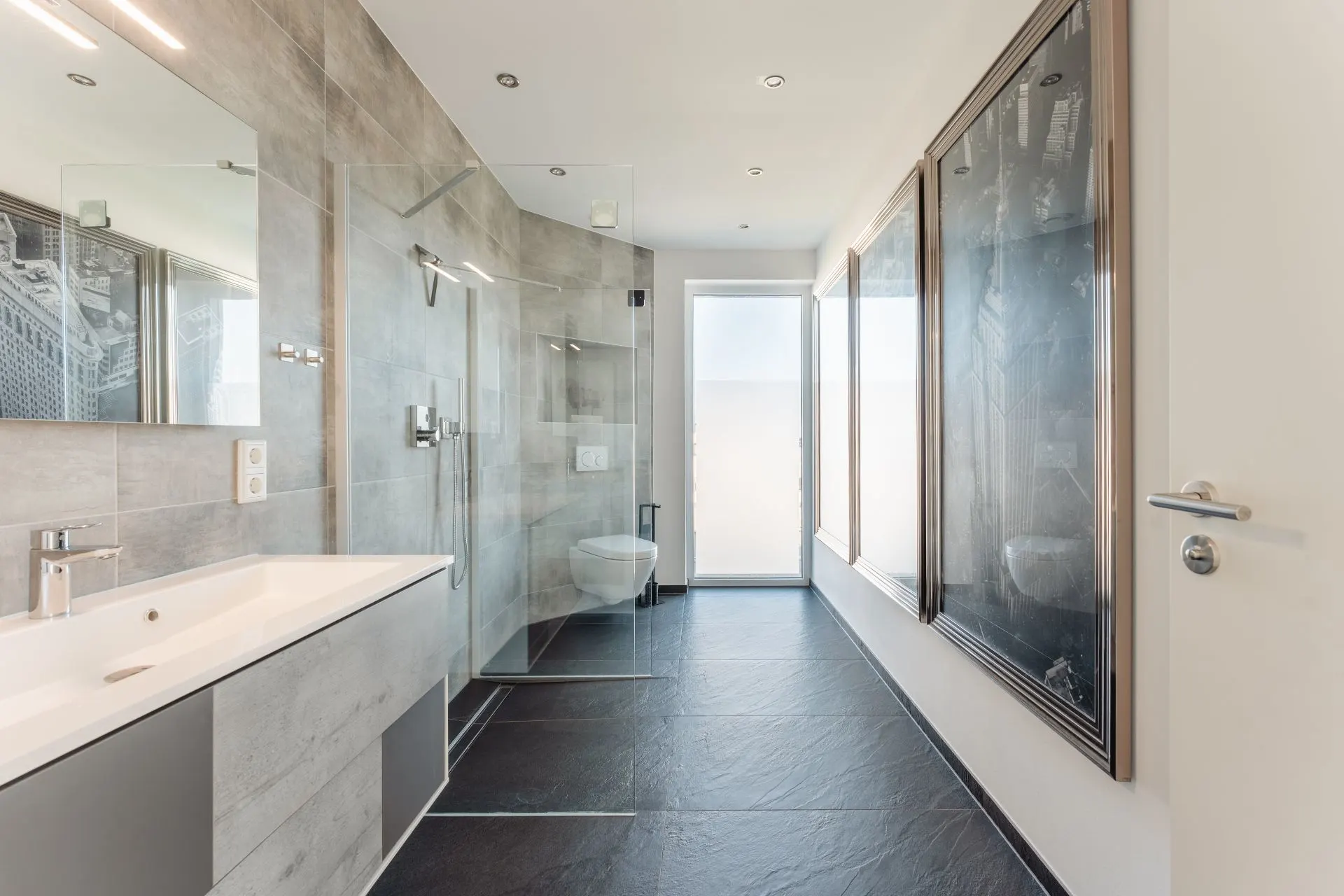 Modernes Badezimmer mit grauen Fliesen, großer Dusche und breitem Waschbecken.