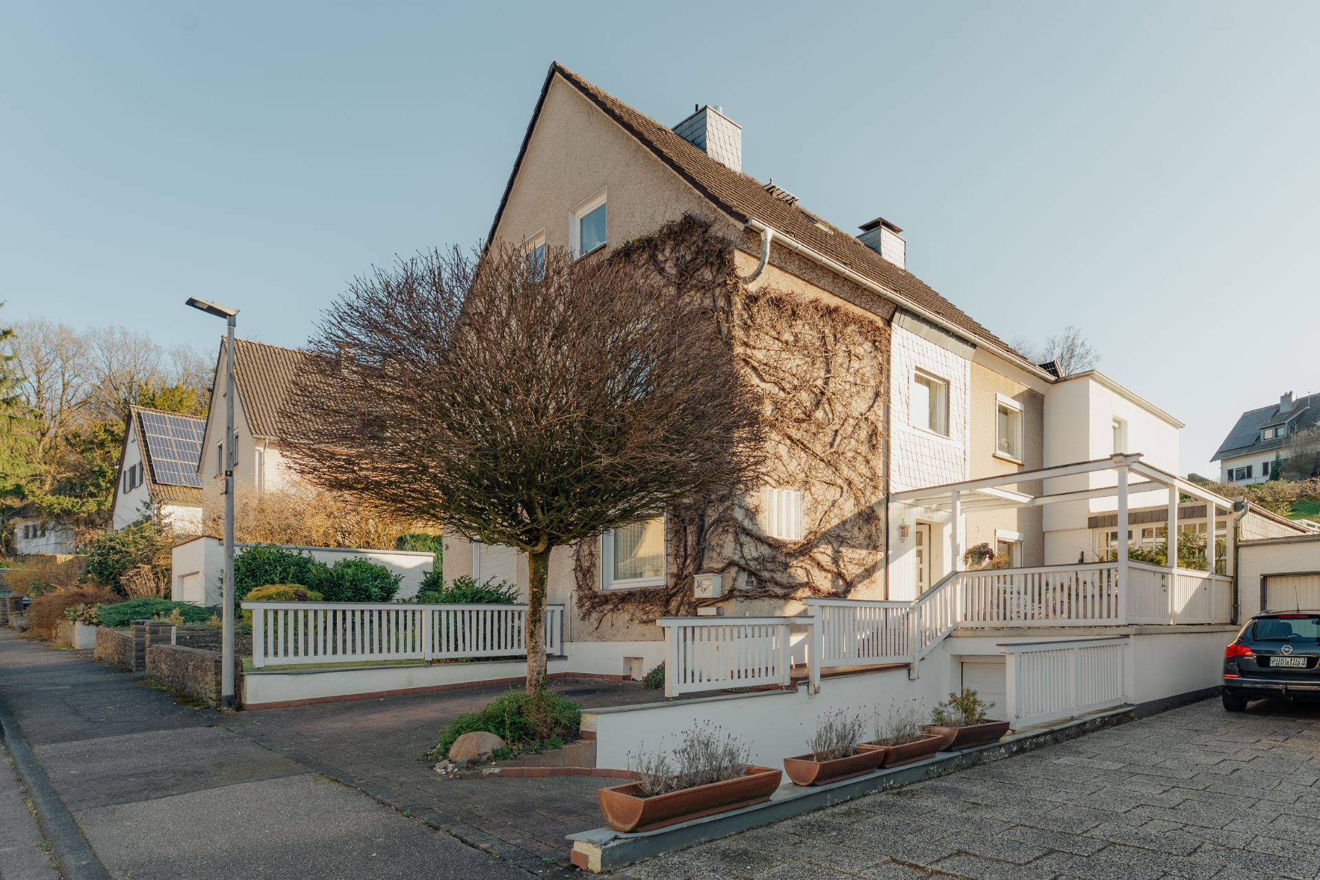 Zweistöckiges Wohnhaus mit Vorgarten, Terrasse, Baum und weißem Zaun an einer ruhigen Straße.