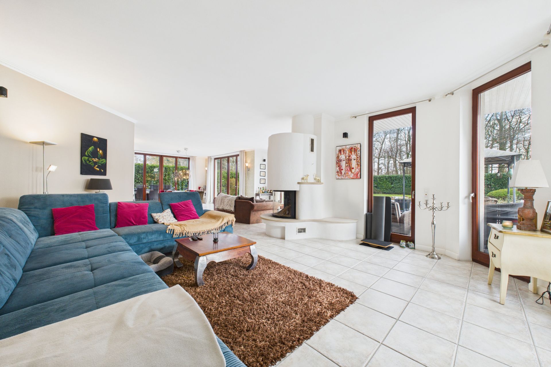 Helles Wohnzimmer mit blauem Sofa, Kamin, großen Fenstern und braunem Teppich.
