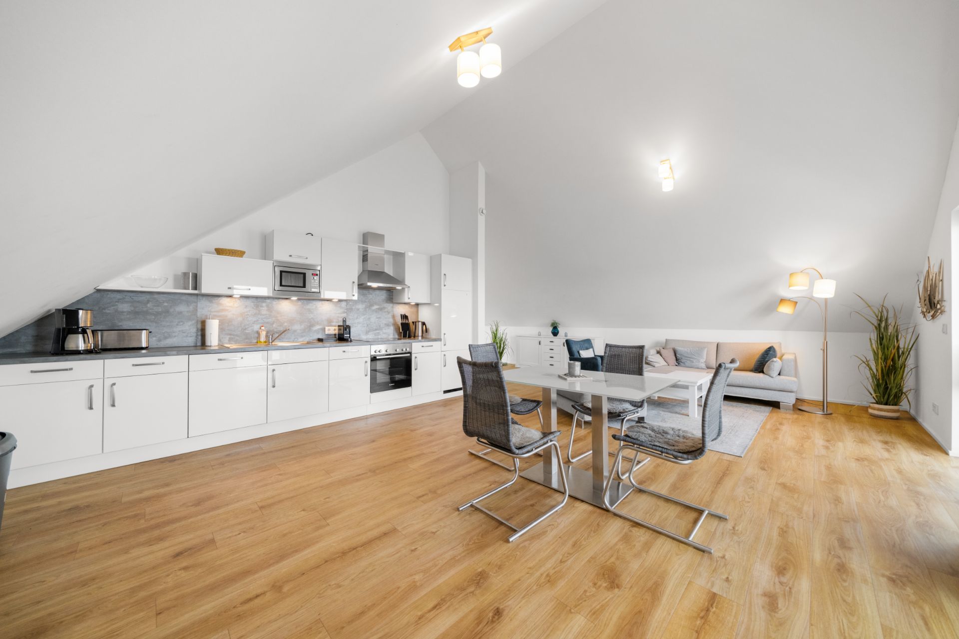 Helles Wohnzimmer mit offener Küche, Esstisch, Stühlen und Sofa auf Holzfußboden.