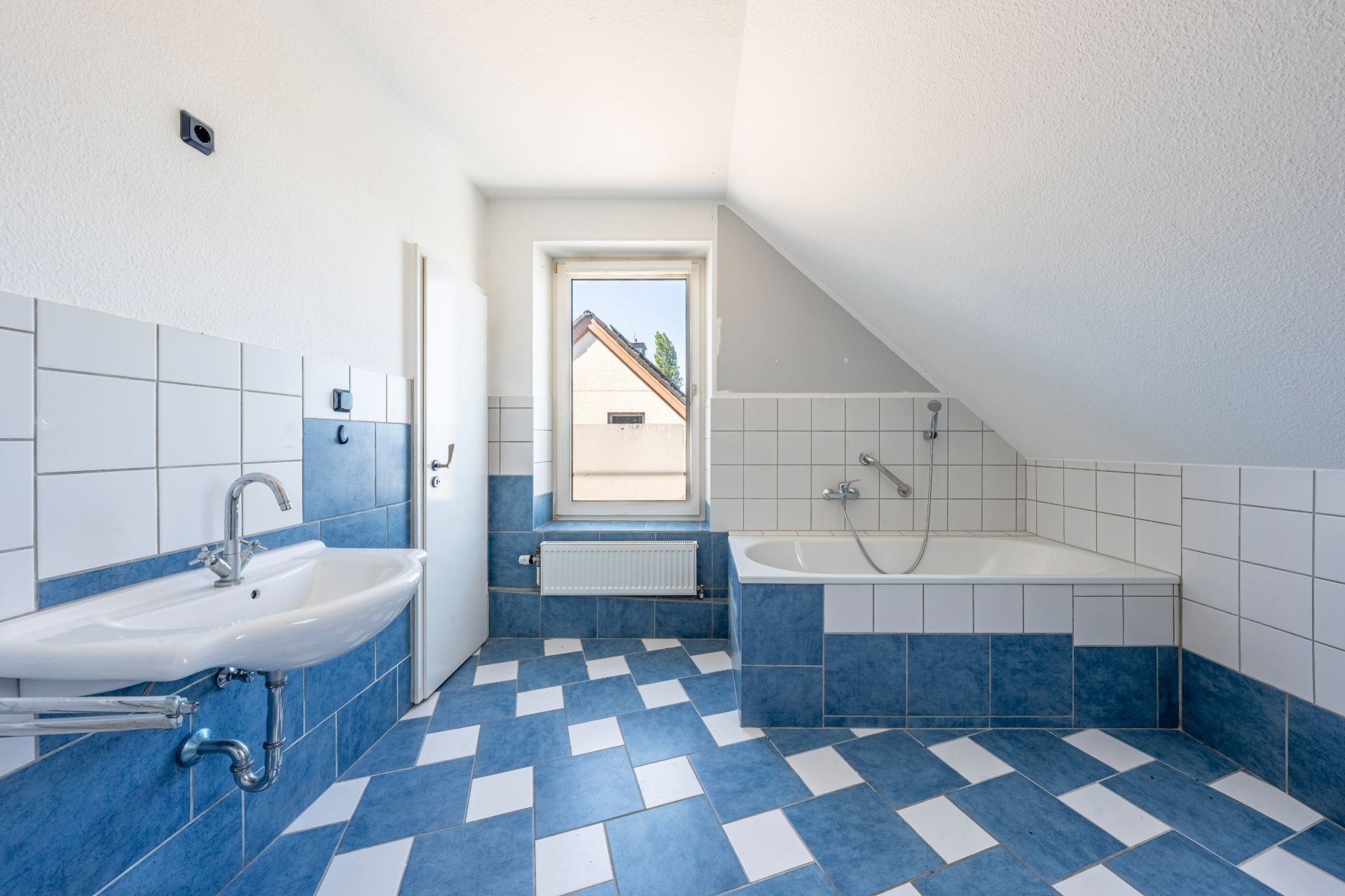 Helles Badezimmer mit blauen und weißen Fliesen, Badewanne, Waschbecken und Fenster.